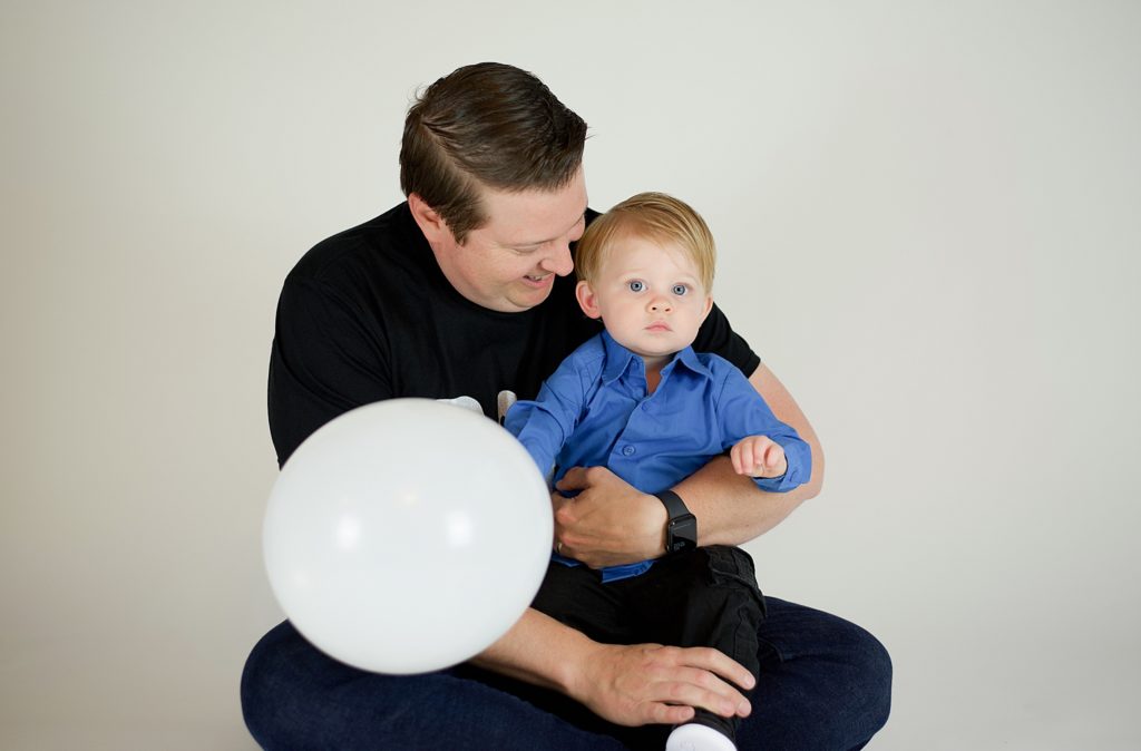 dad and son play with white balloon during studio first birthday cake smash