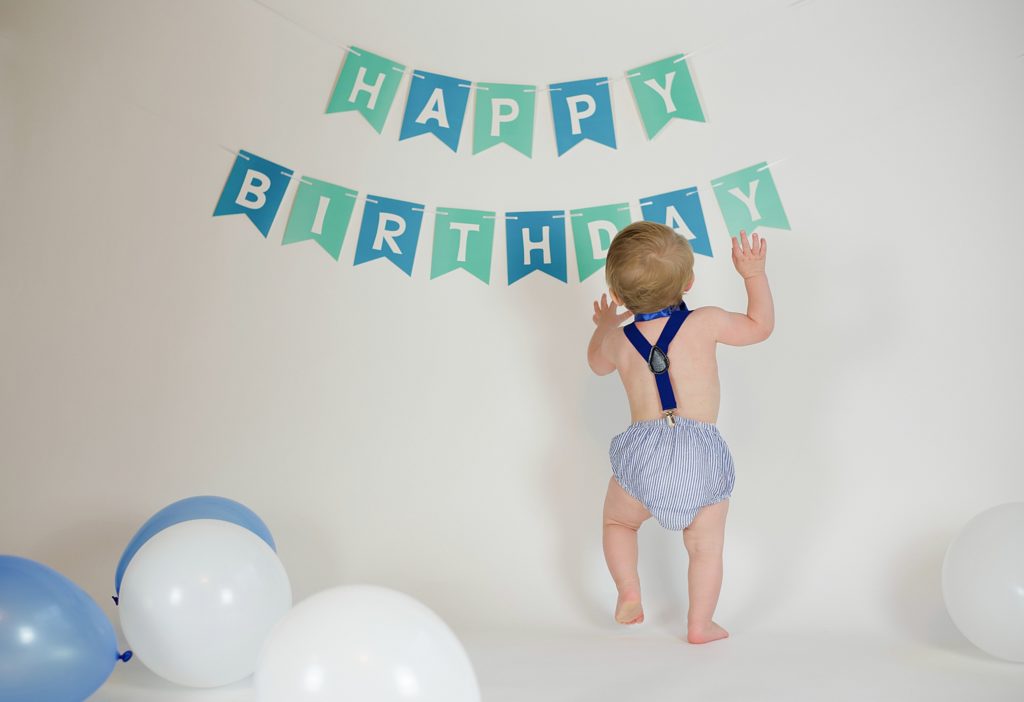 toddler reaches up for happy birthday banner in studio