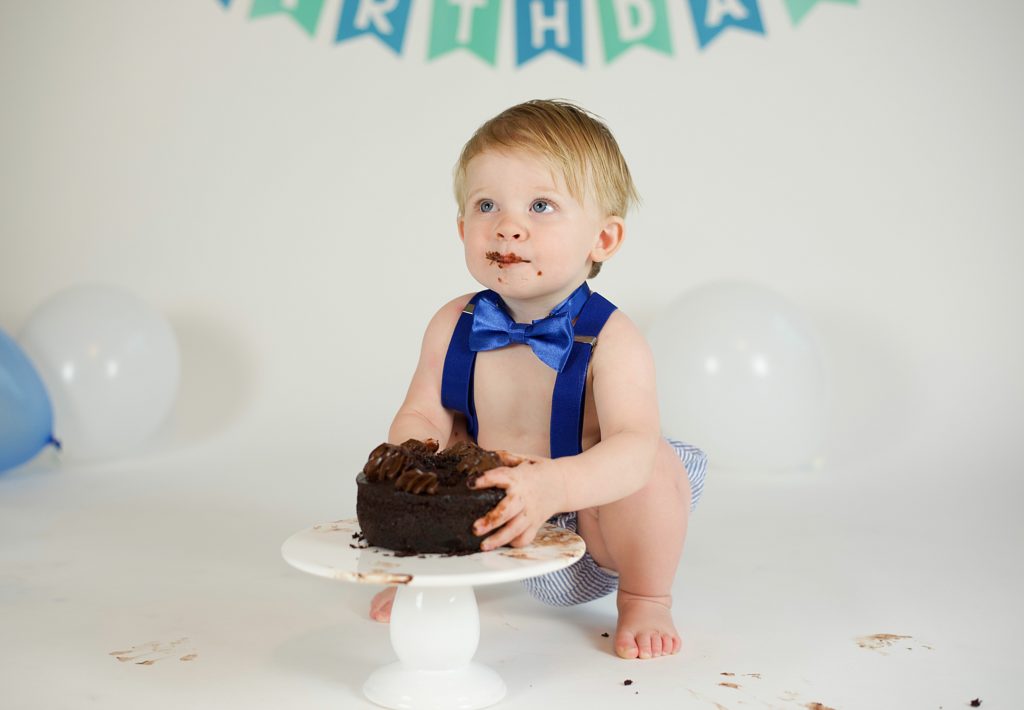 toddler in blue suspenders plays with chocolate cake 