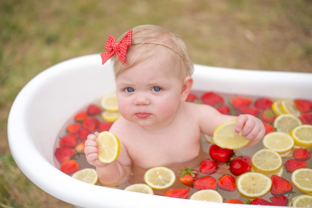 toddler sits in fruit bath for 9 month milestone portraits
