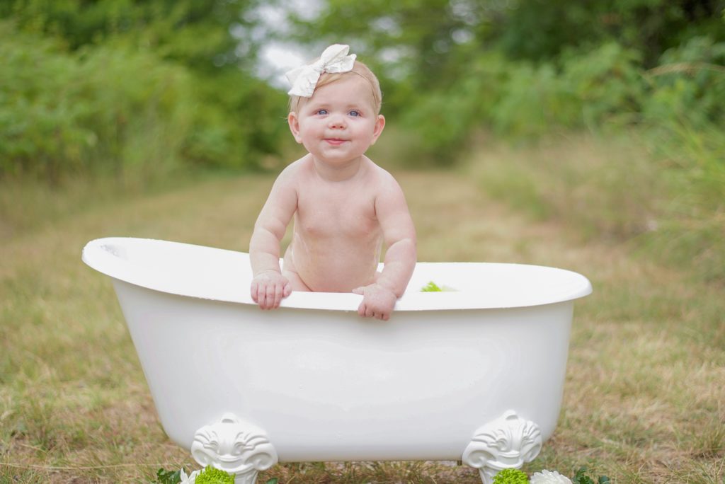 9 month old baby girl stands in tub during Milk Bath Milestone Portraits