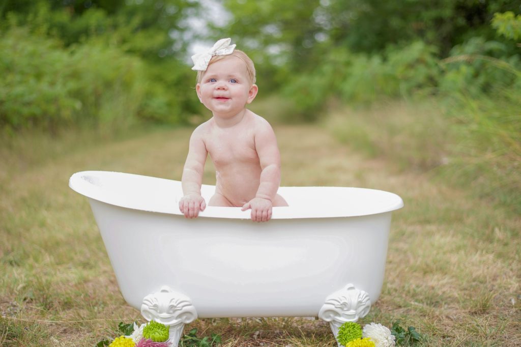 baby stands up in tub during Milk Bath Milestone Portraits