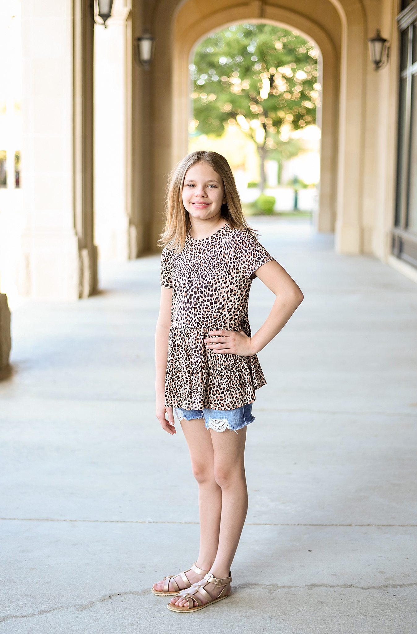 daughter in leopard print shirt poses by building in Frisco TX