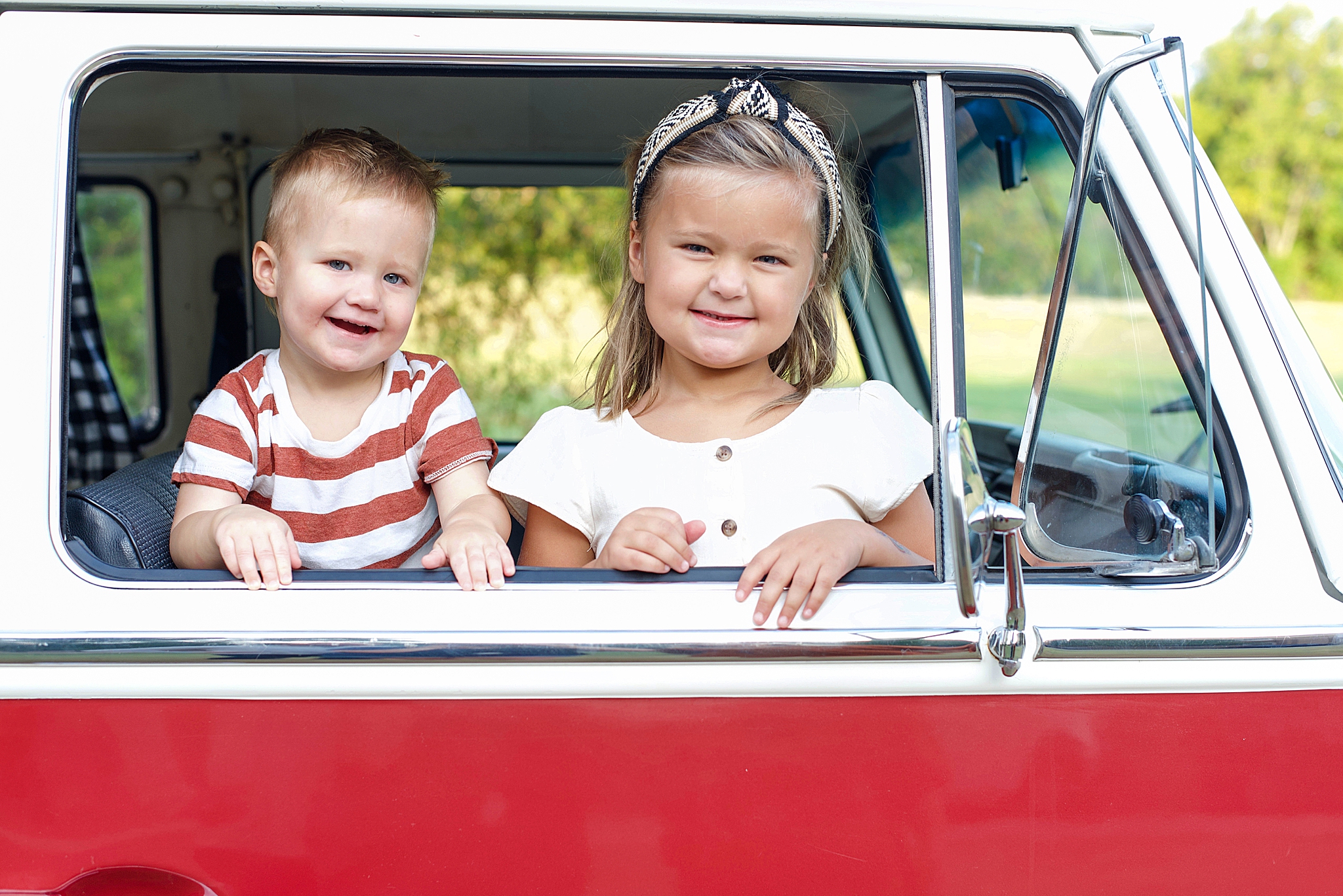 siblings look out window of red VW van