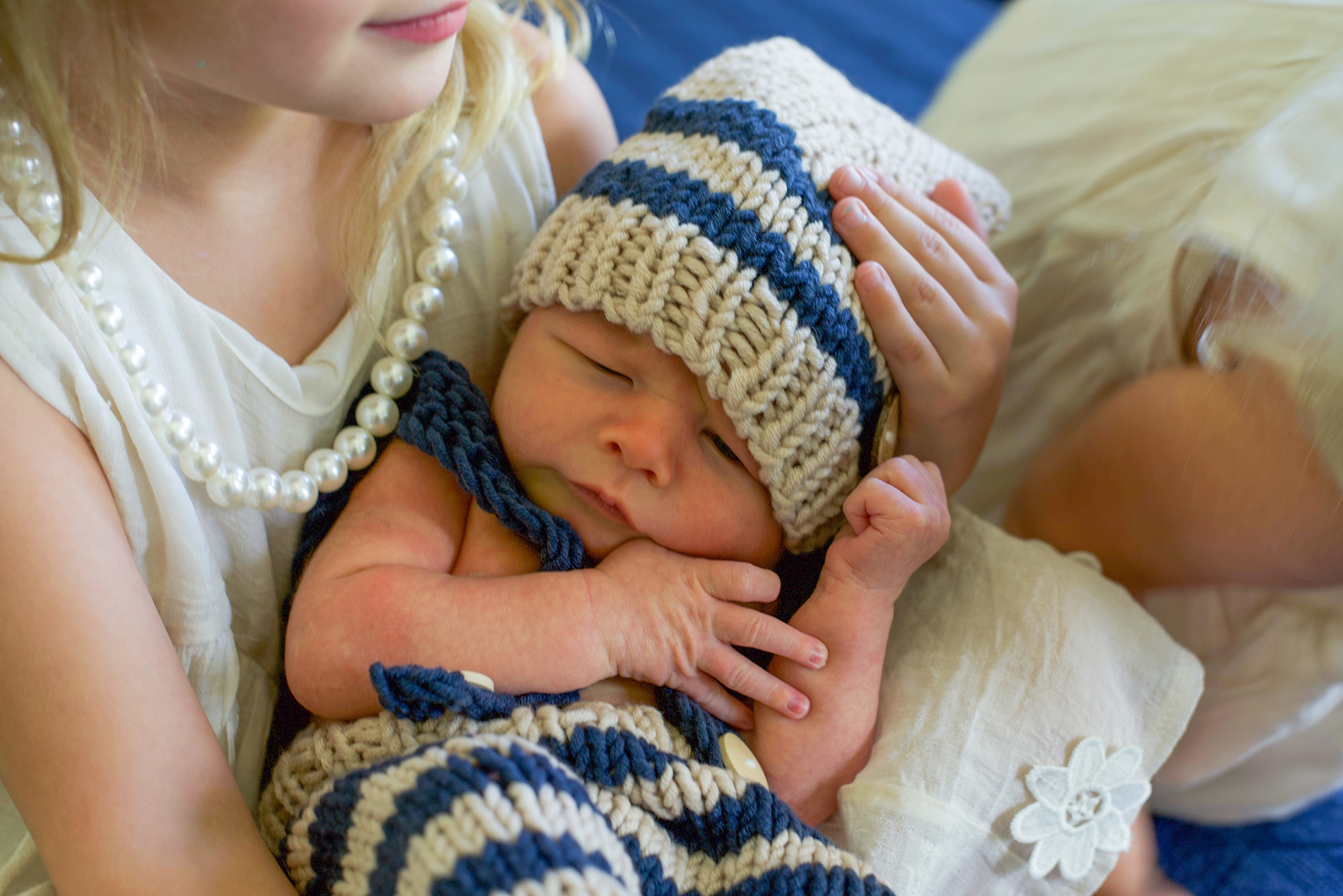 baby in blue and white knit outfit snuggles with big sisters 