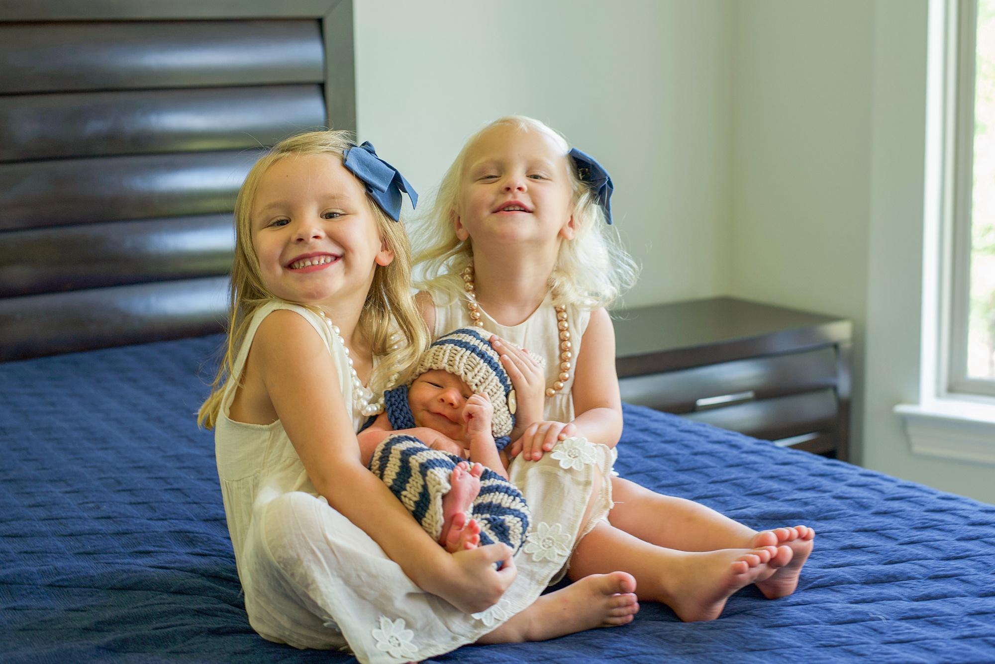 sisters hold baby brother on bed