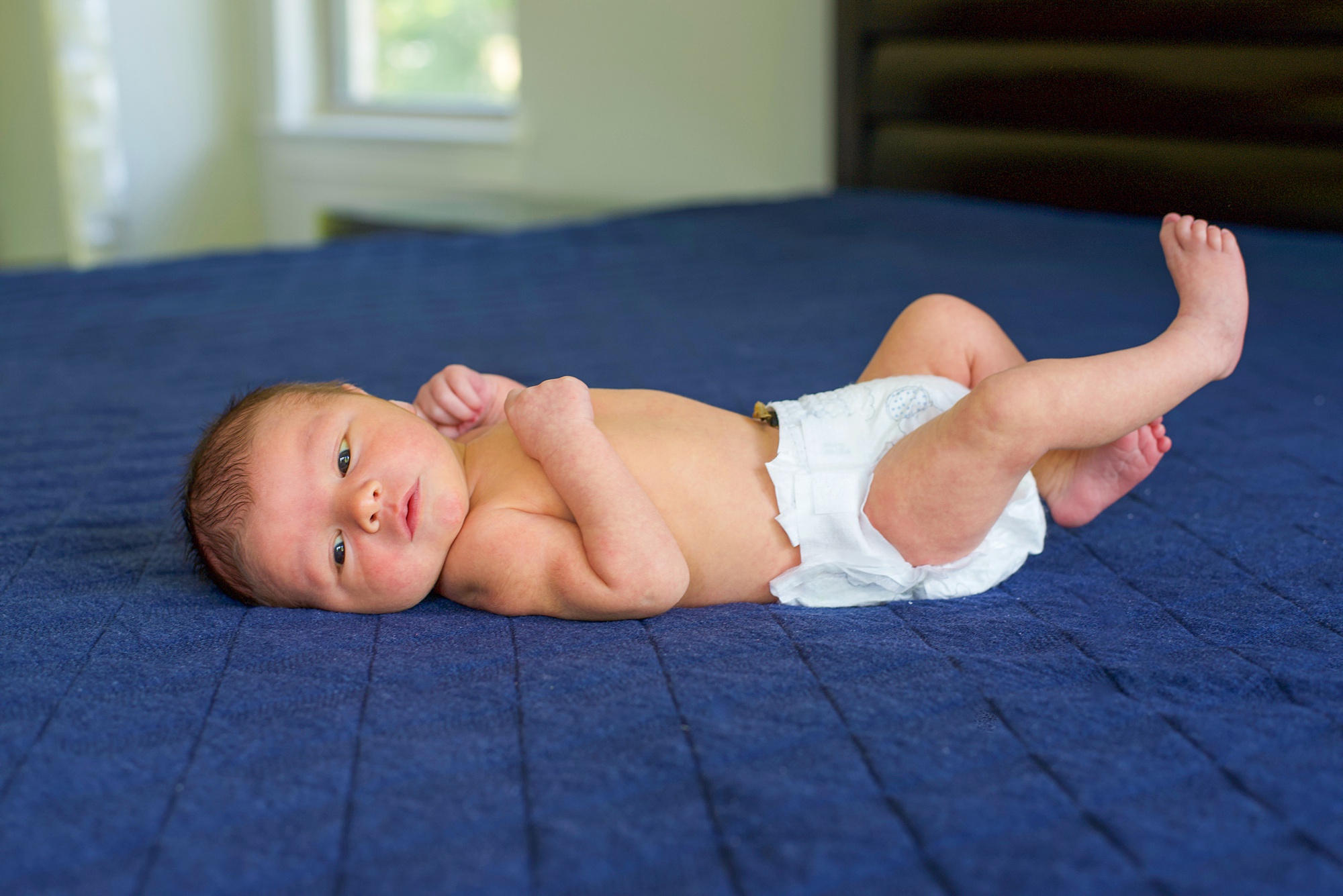 baby in diaper lays on blue comforter 