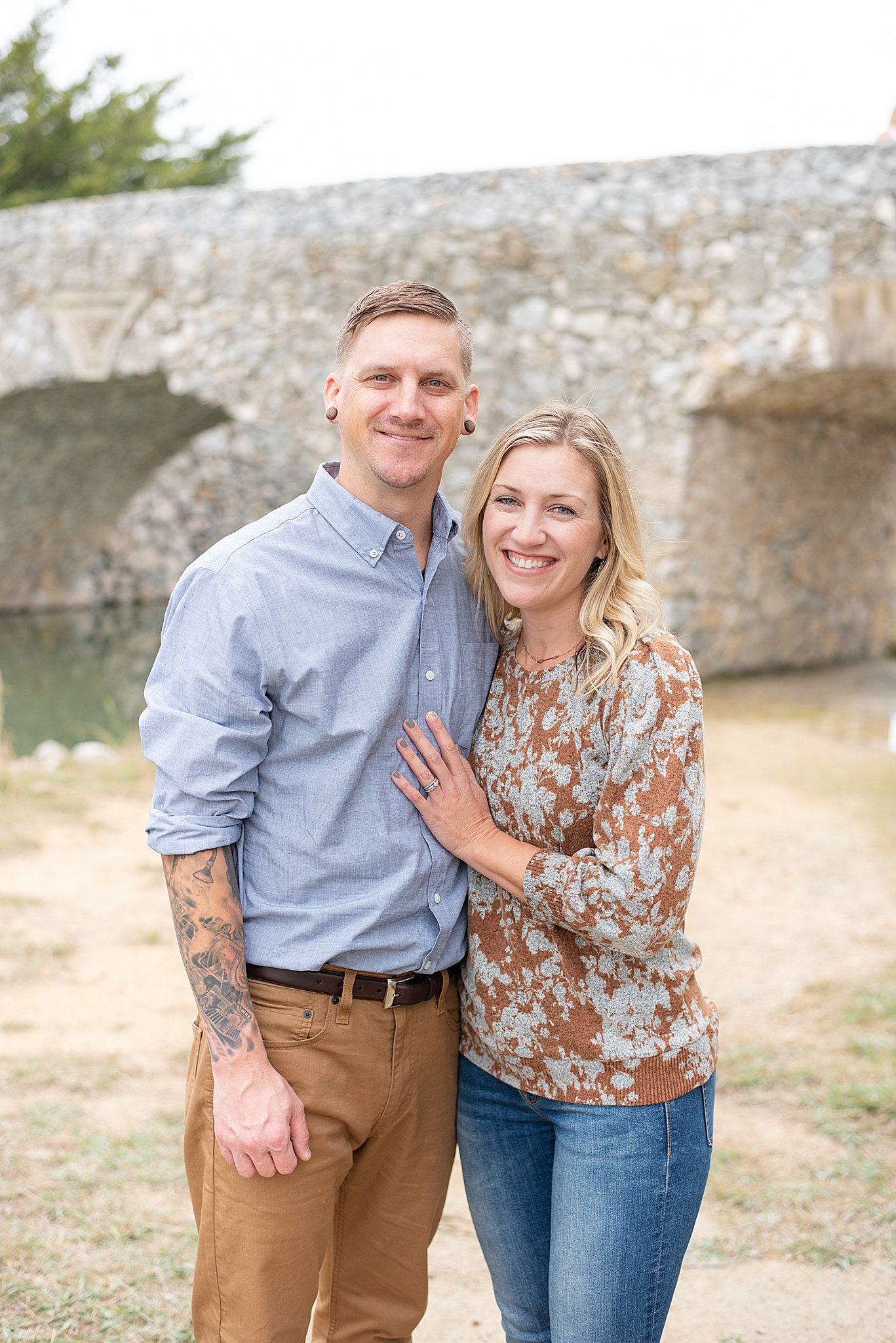 husband and wife pose by stone bridge in Texas