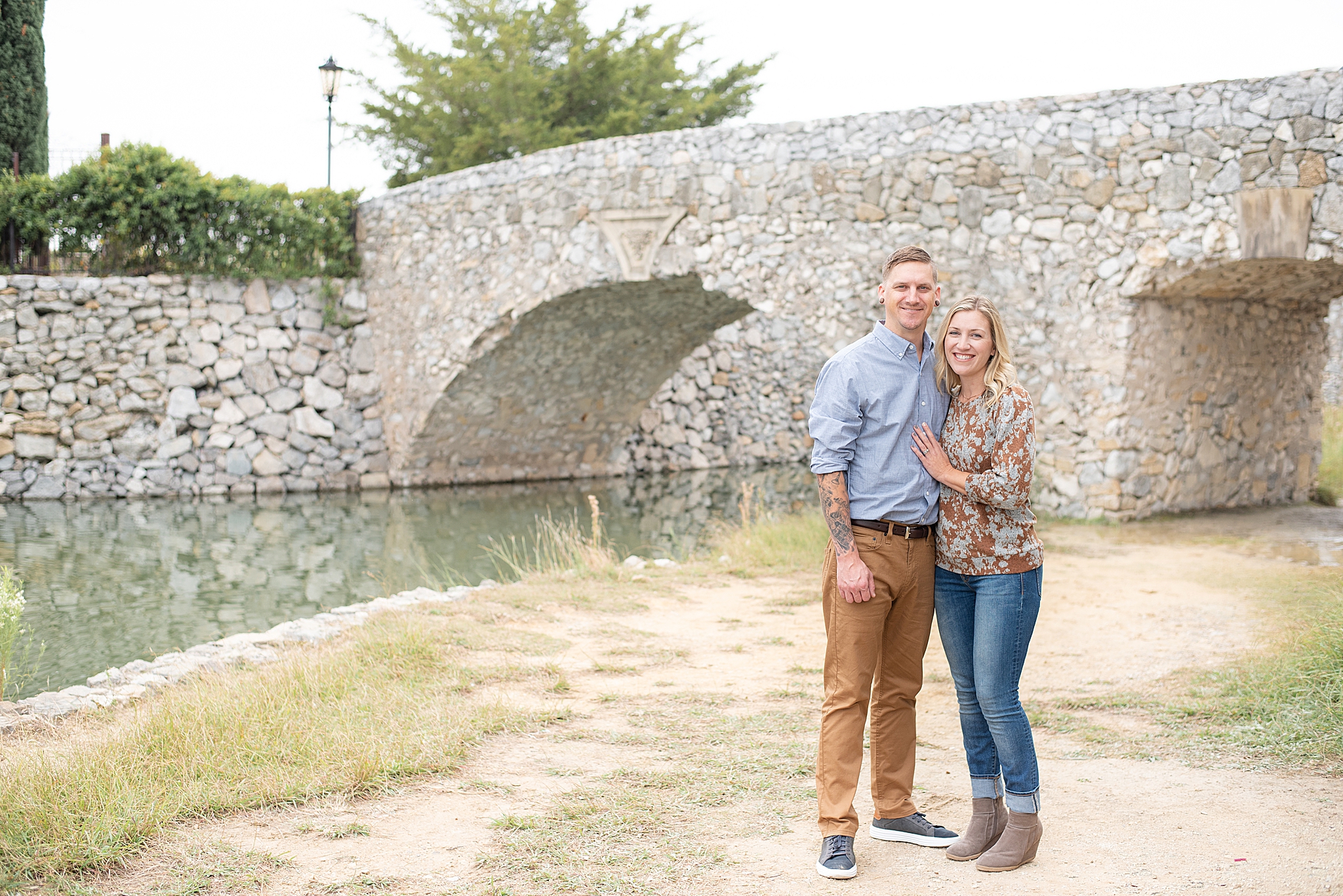 husband and wife pose by stone bridge in Texas