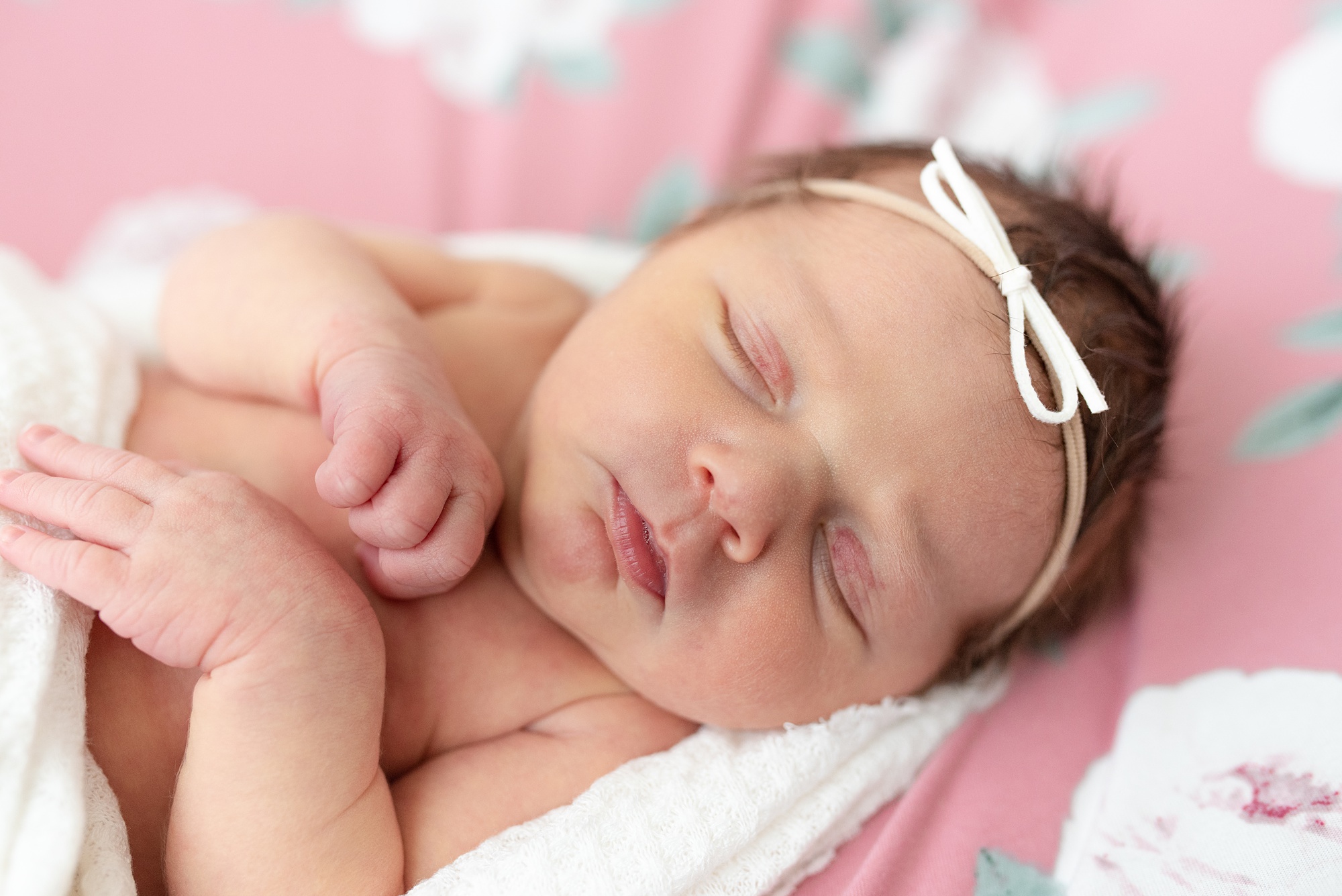 baby lays on pink sheets with flowers during newborn session at home 
