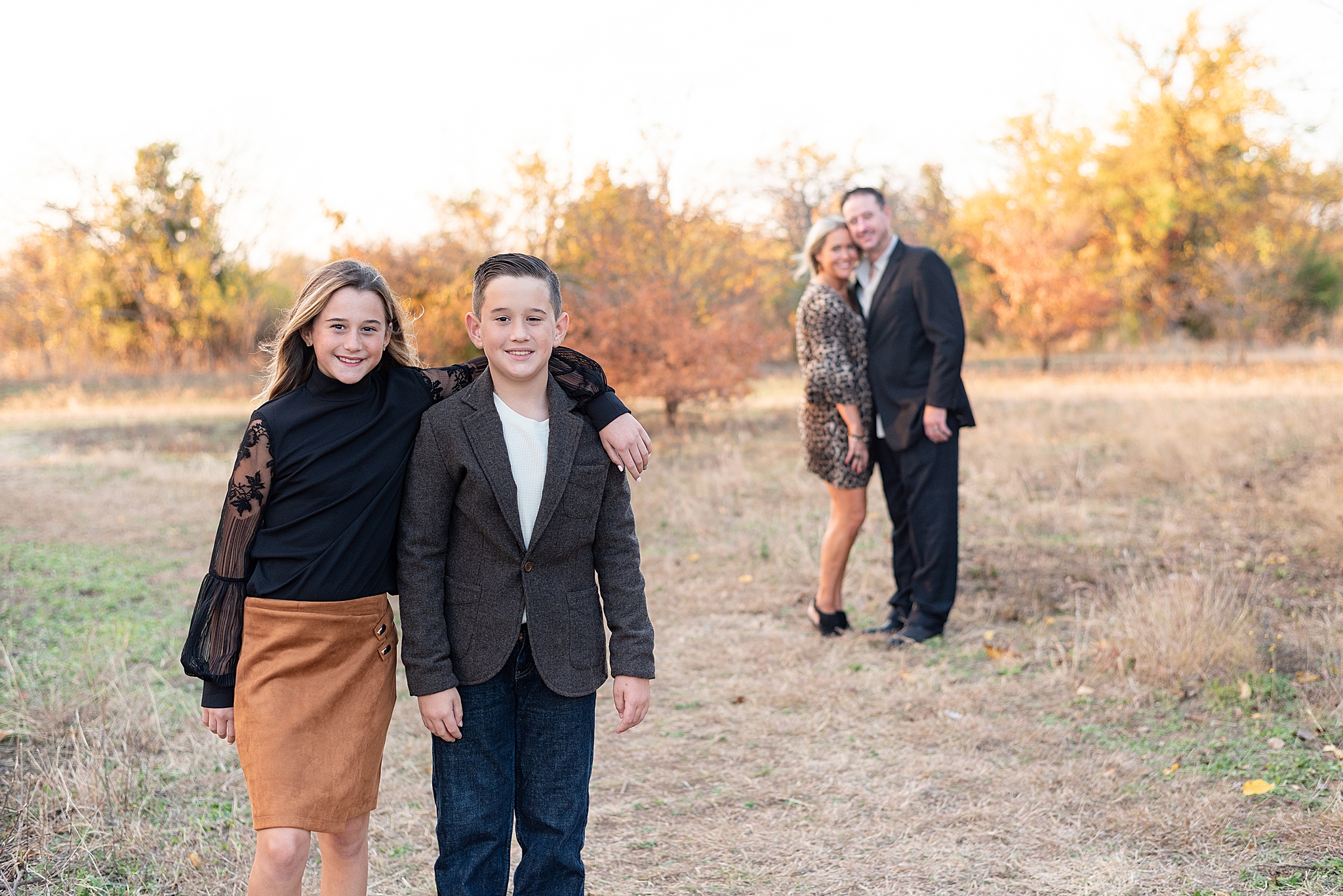 siblings hug with parents in the back during Frisco Field Mini Sessions