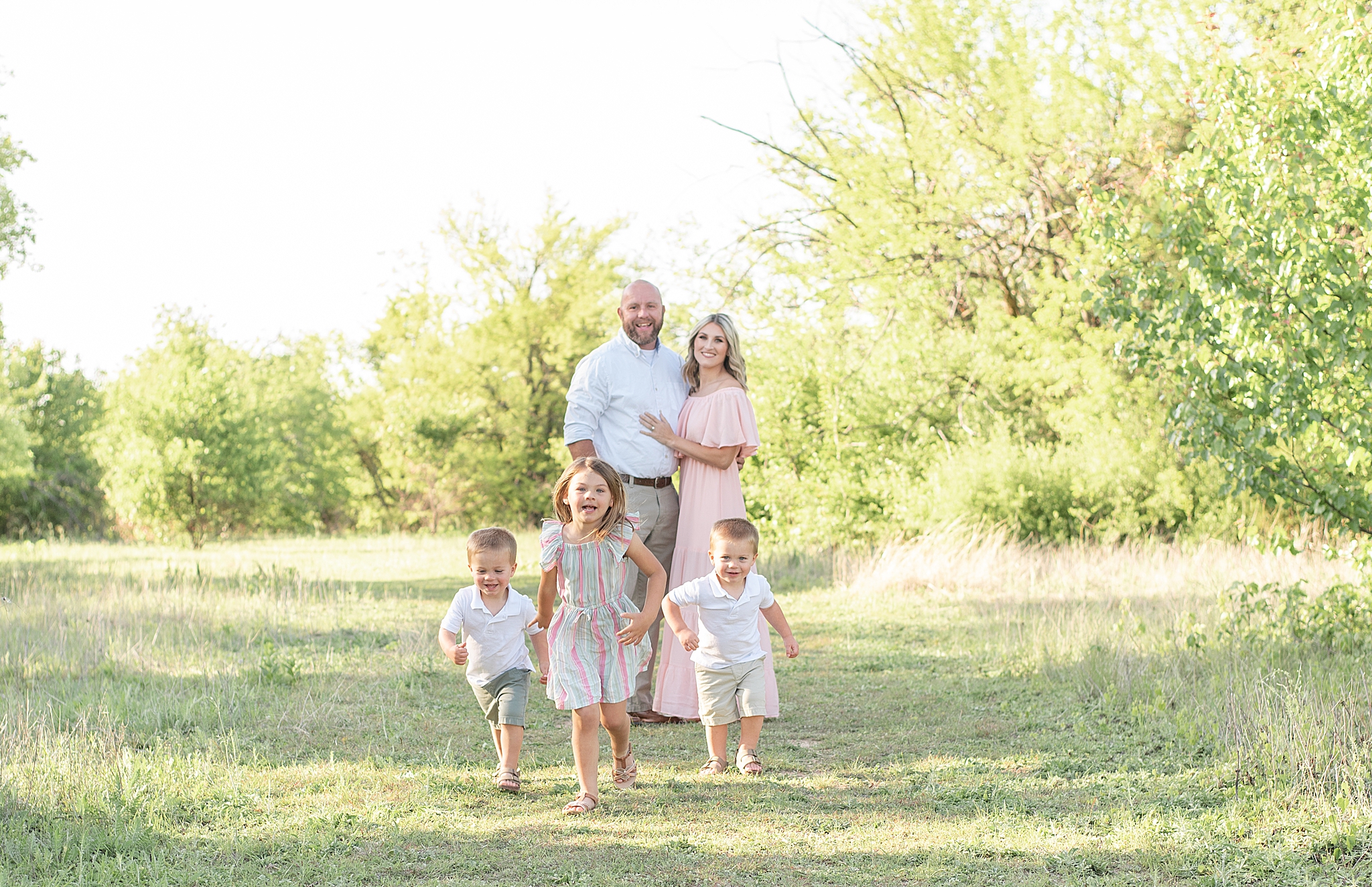 parents hug while three kids run during Frisco Field Family + Mommy and Me Session