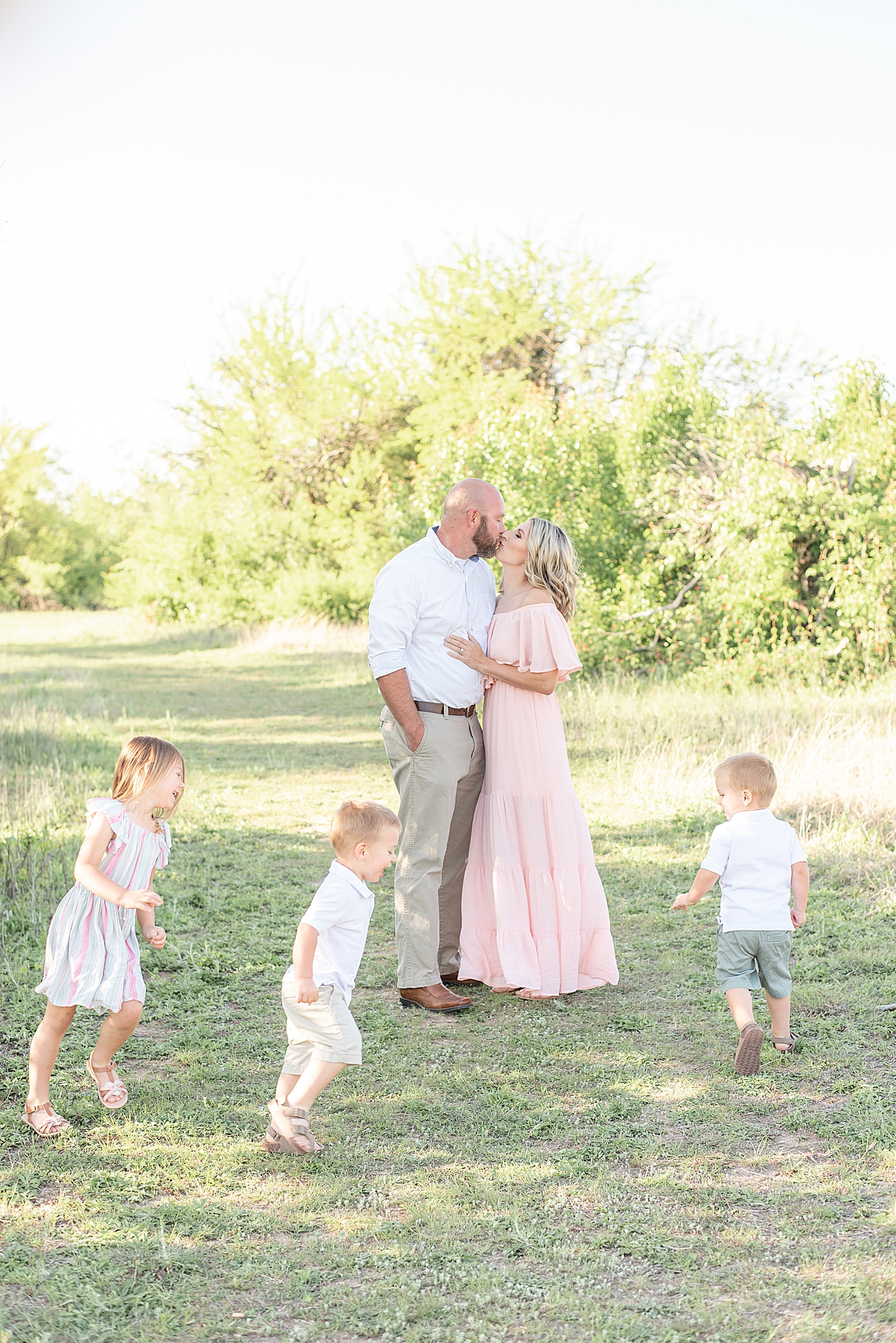 parents kiss while kids run around them during TX family photos
