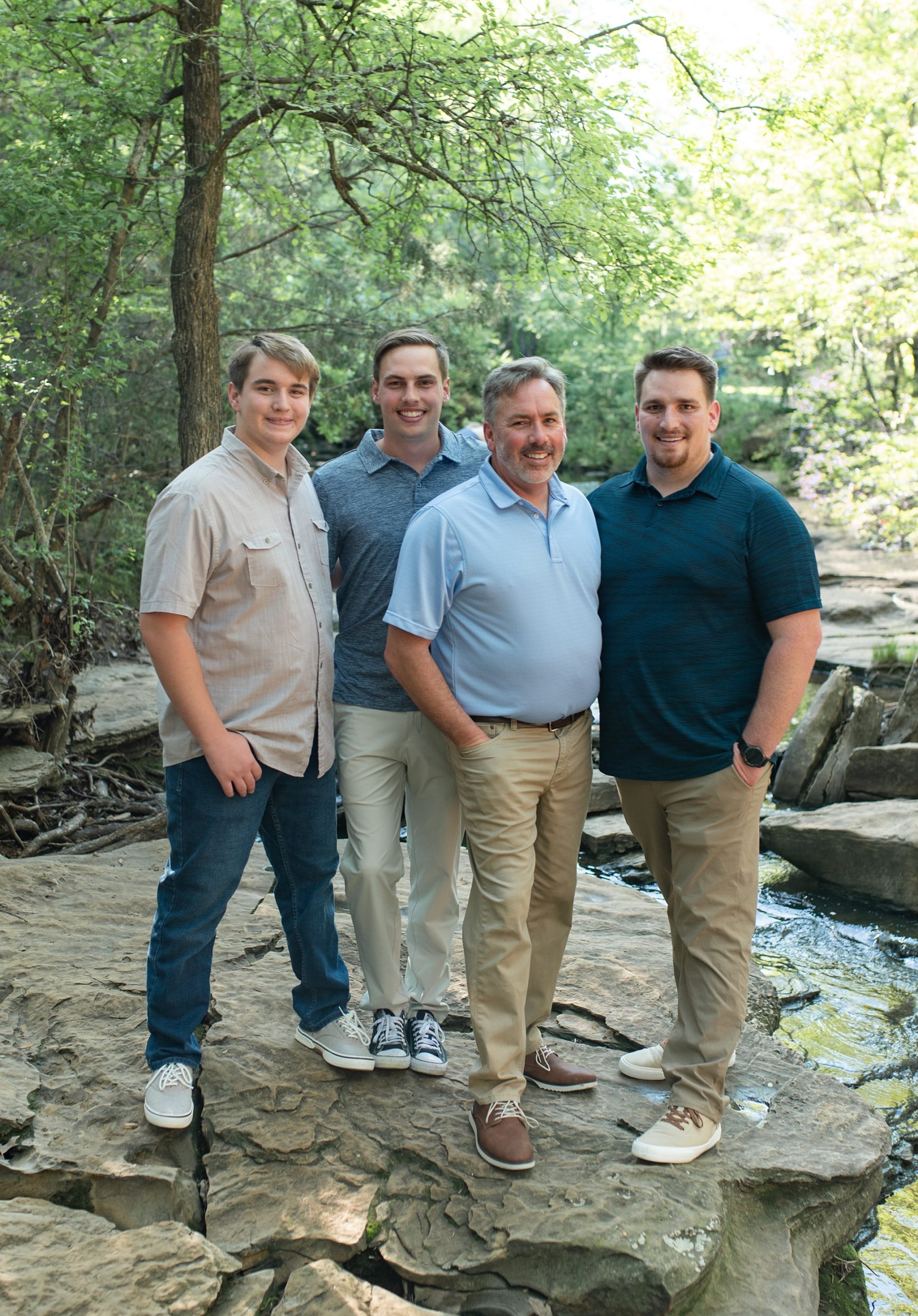 dad poses with three sons on rock bed at Stone Creek Park
