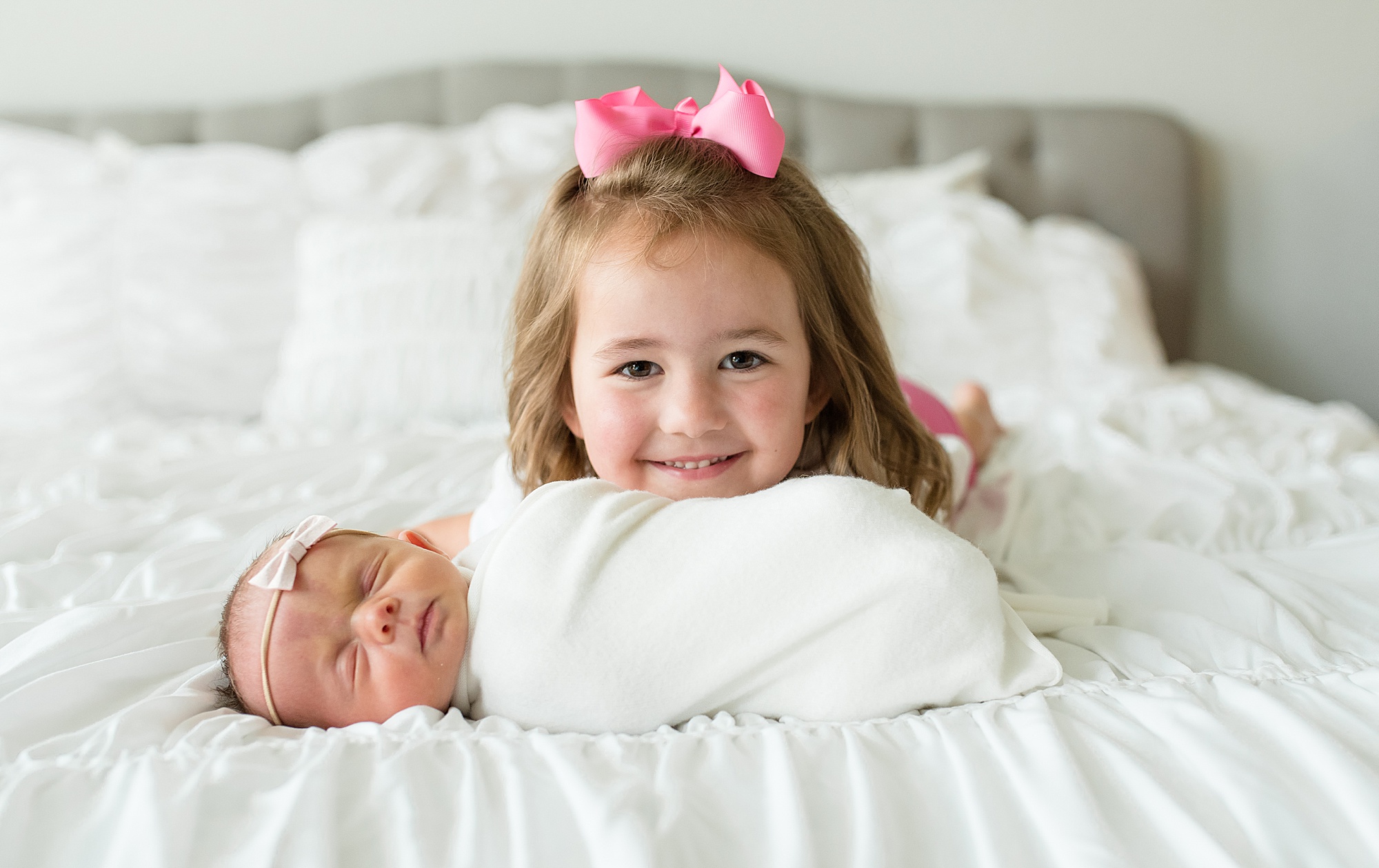 girl lays with newborn sister on bed during in-home lifestyle newborn session