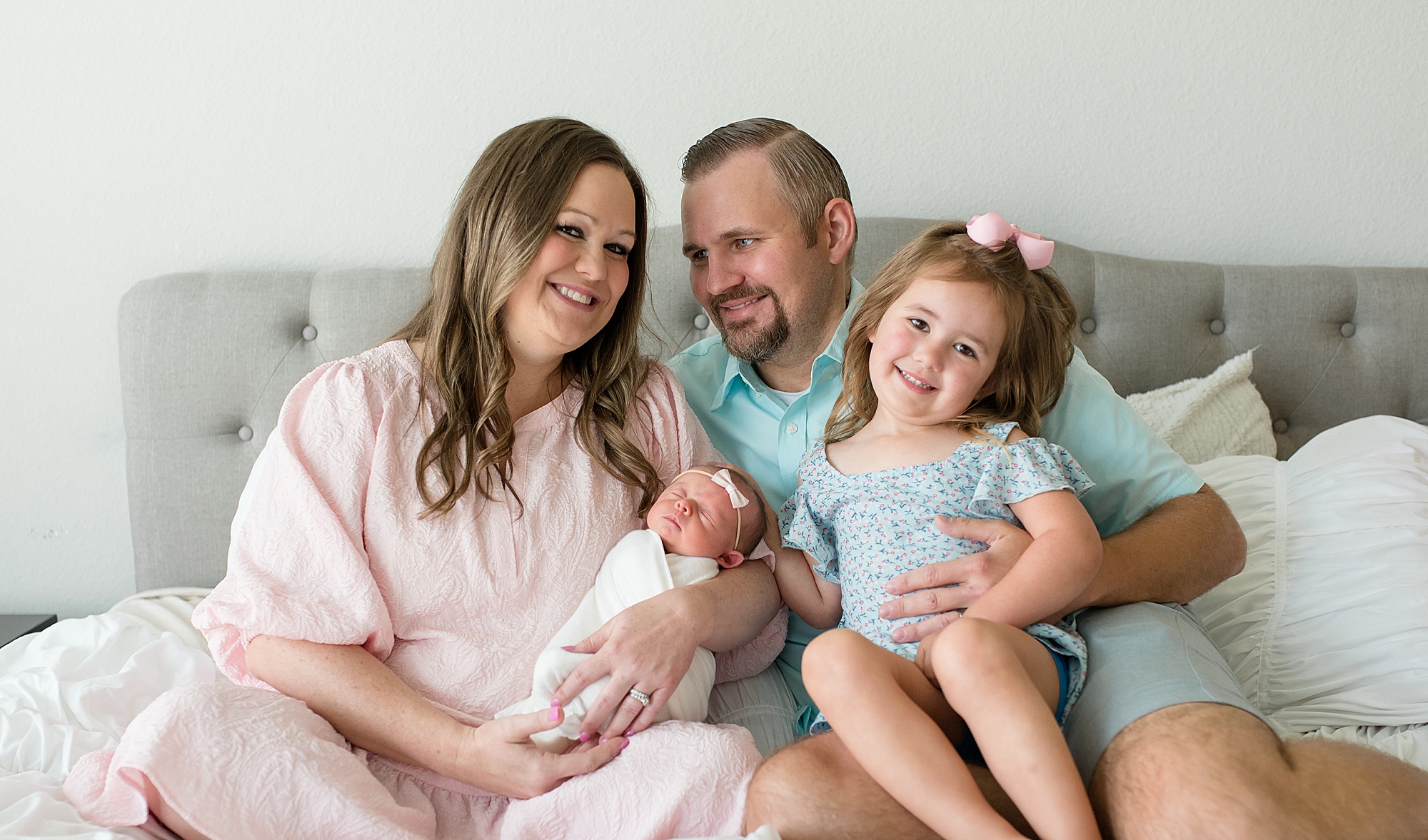 family of four sits on grey bed during TX newborn photos