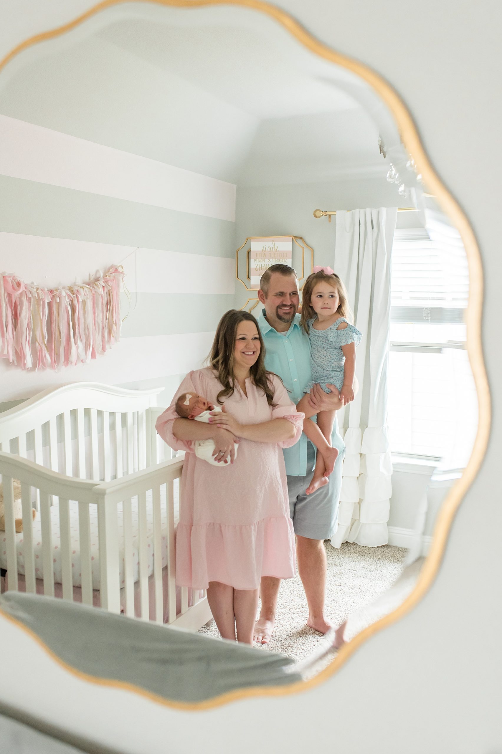 family of four poses in mirror with gold frame during in-home lifestyle newborn session