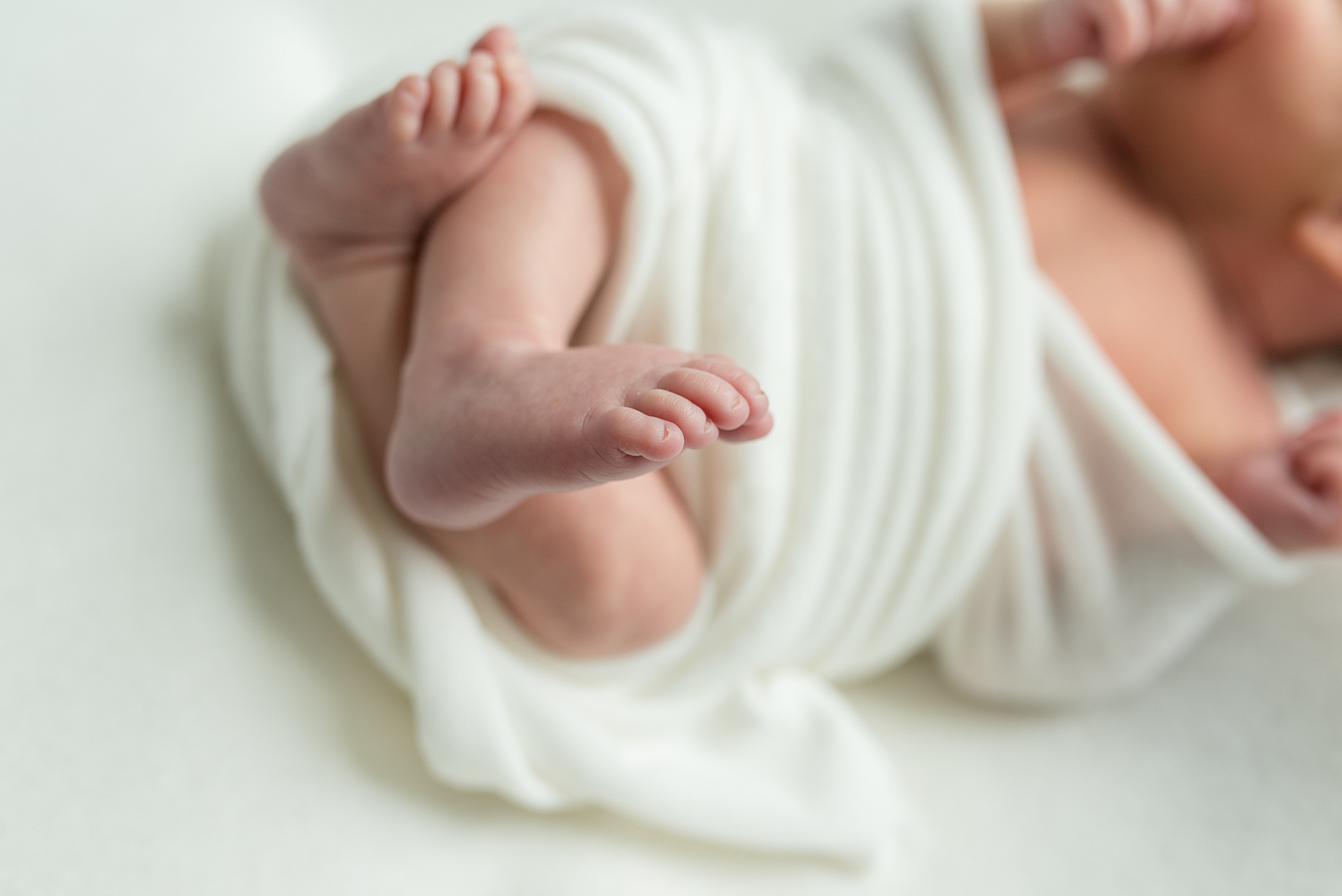 baby sticks feet out of white wrap during in-home lifestyle newborn session