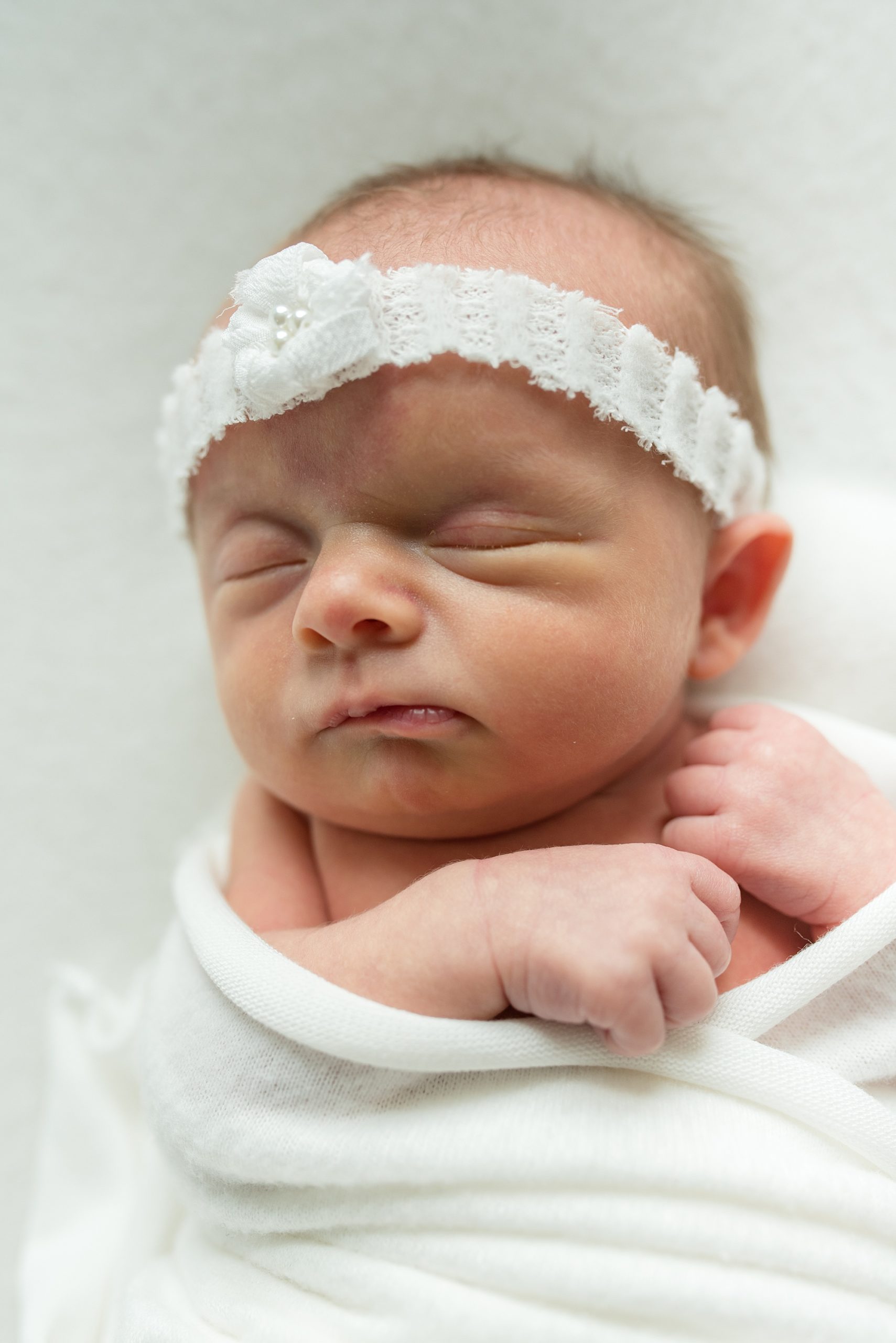 baby girl in white wrap with white headband sleeps
