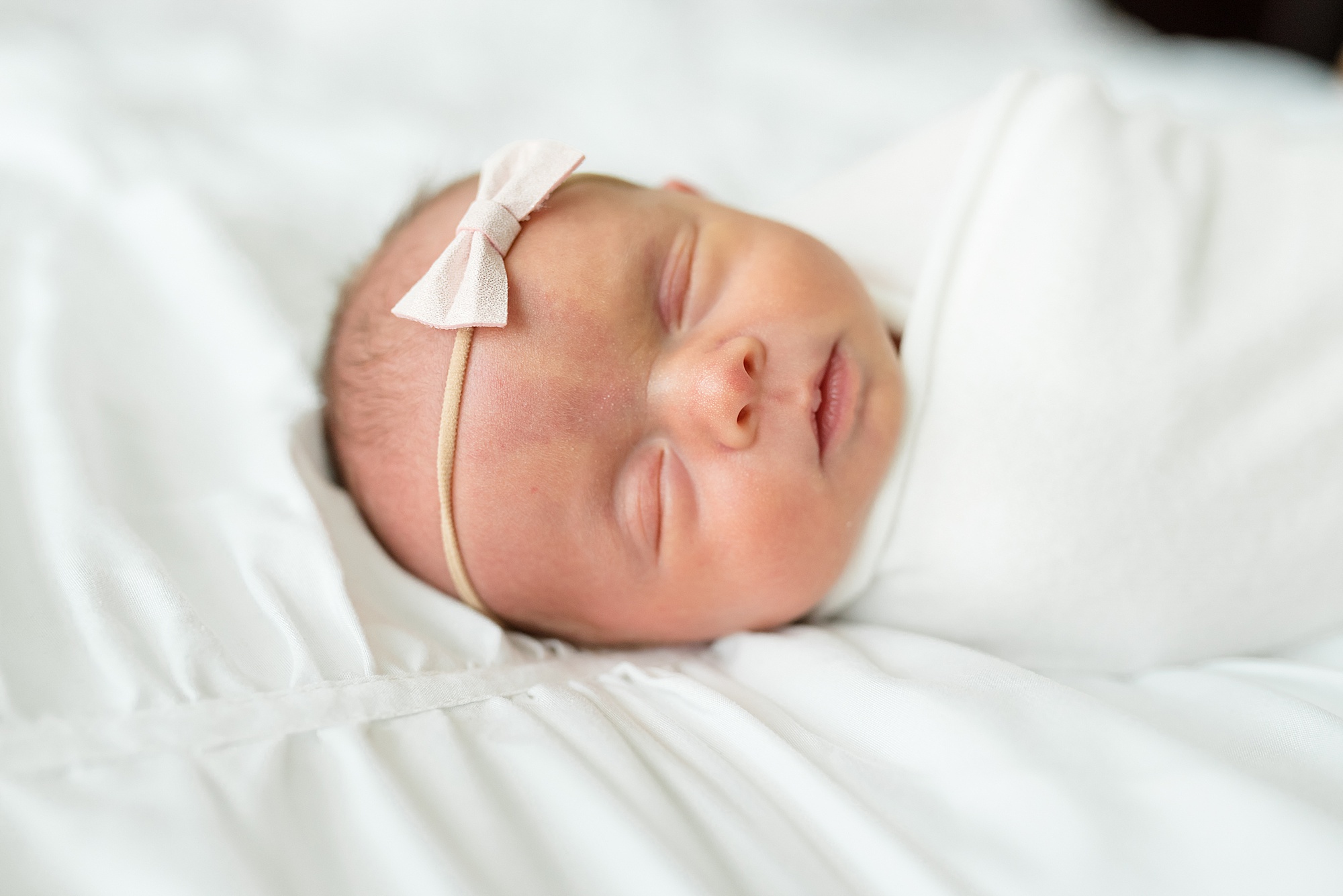 baby girl lays on sheets with white bow during newborn photos at home 
