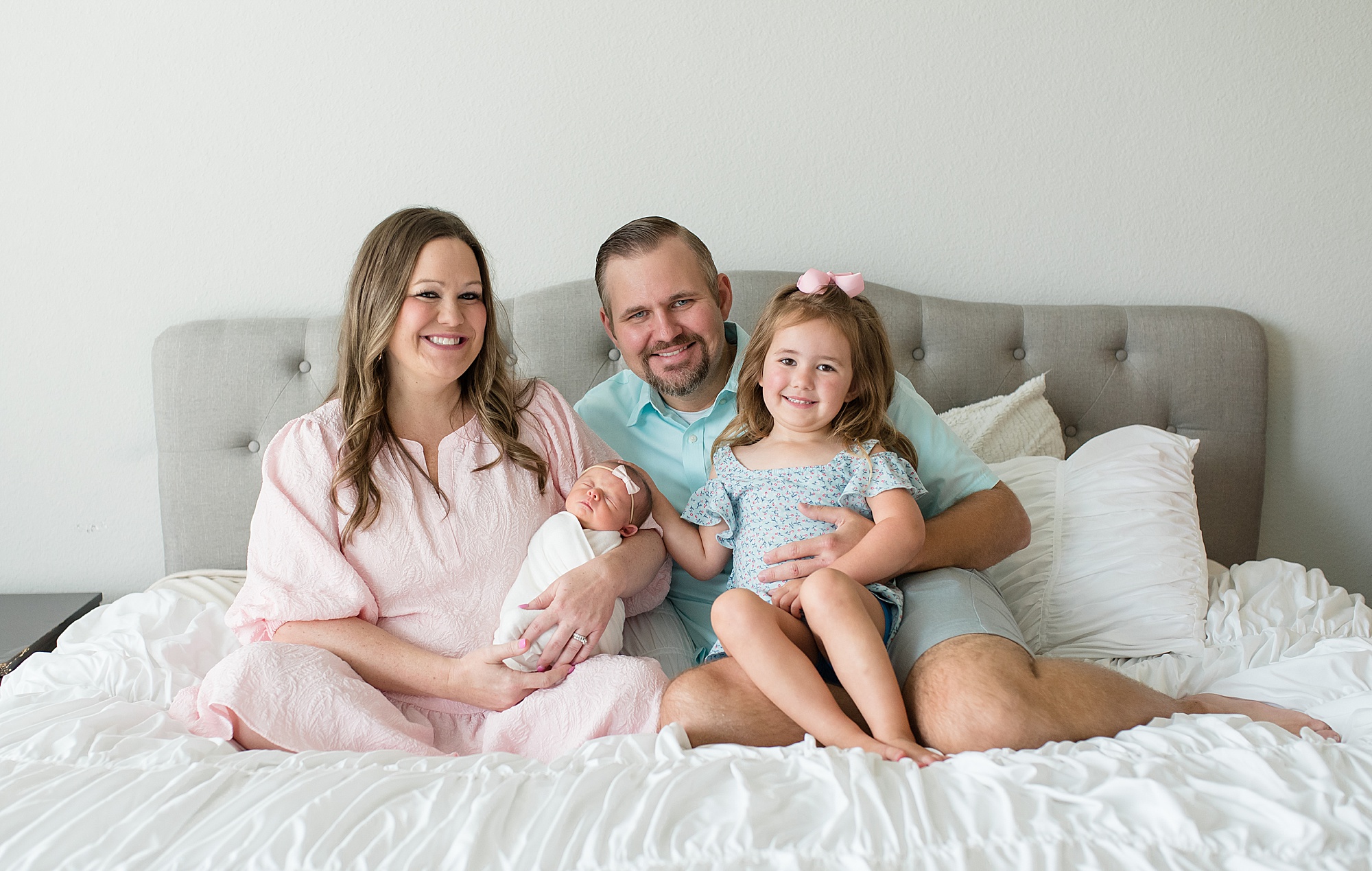 family of four sits on bed during in-home lifestyle newborn session