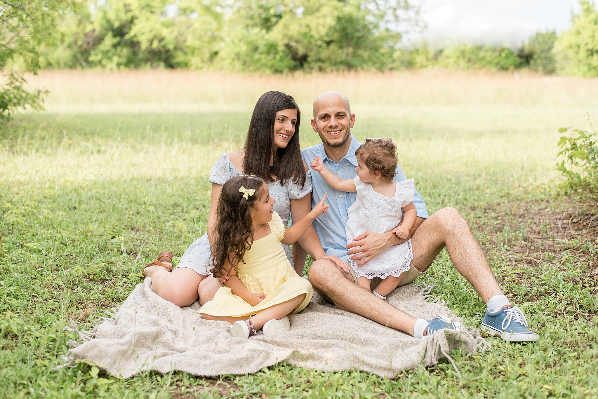 daughters play sitting on dad and mom's lap during family photos