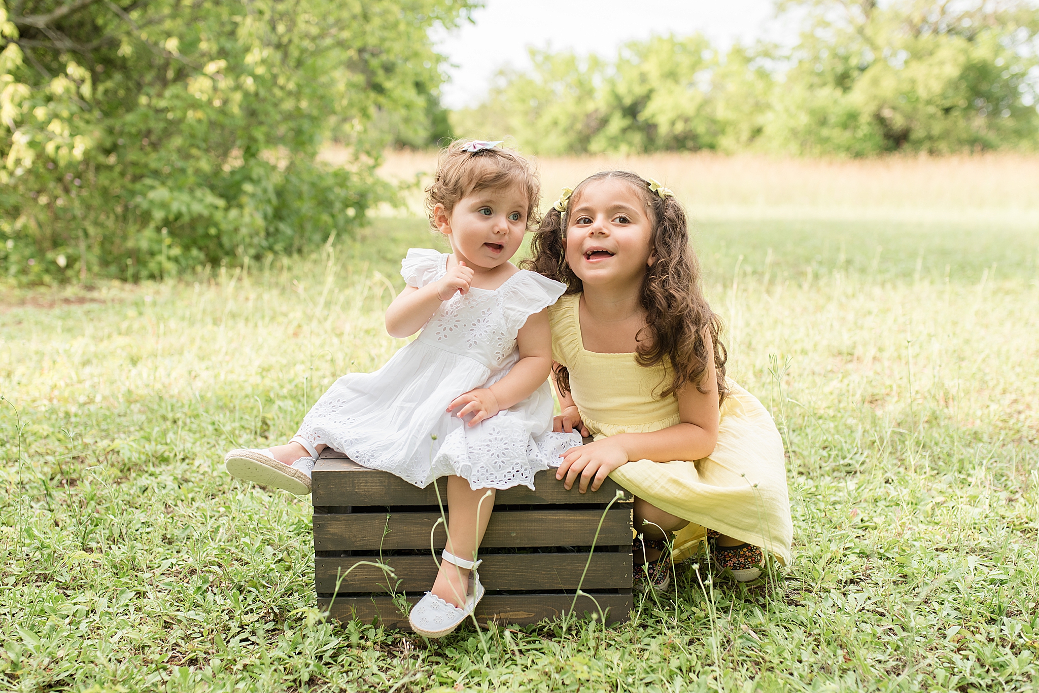sisters sit on wooden box during Milestone Portraits in Frisco