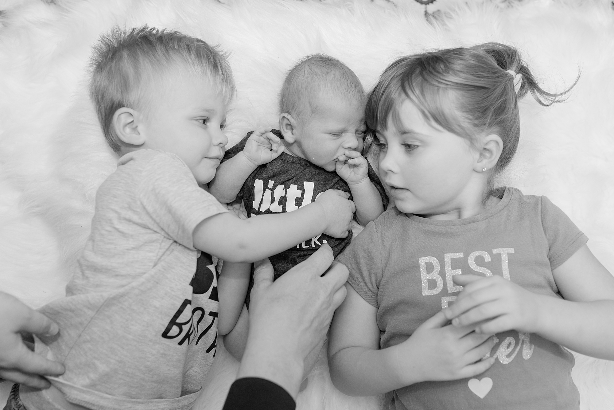 3 siblings lay together on the bed loving on their little brother