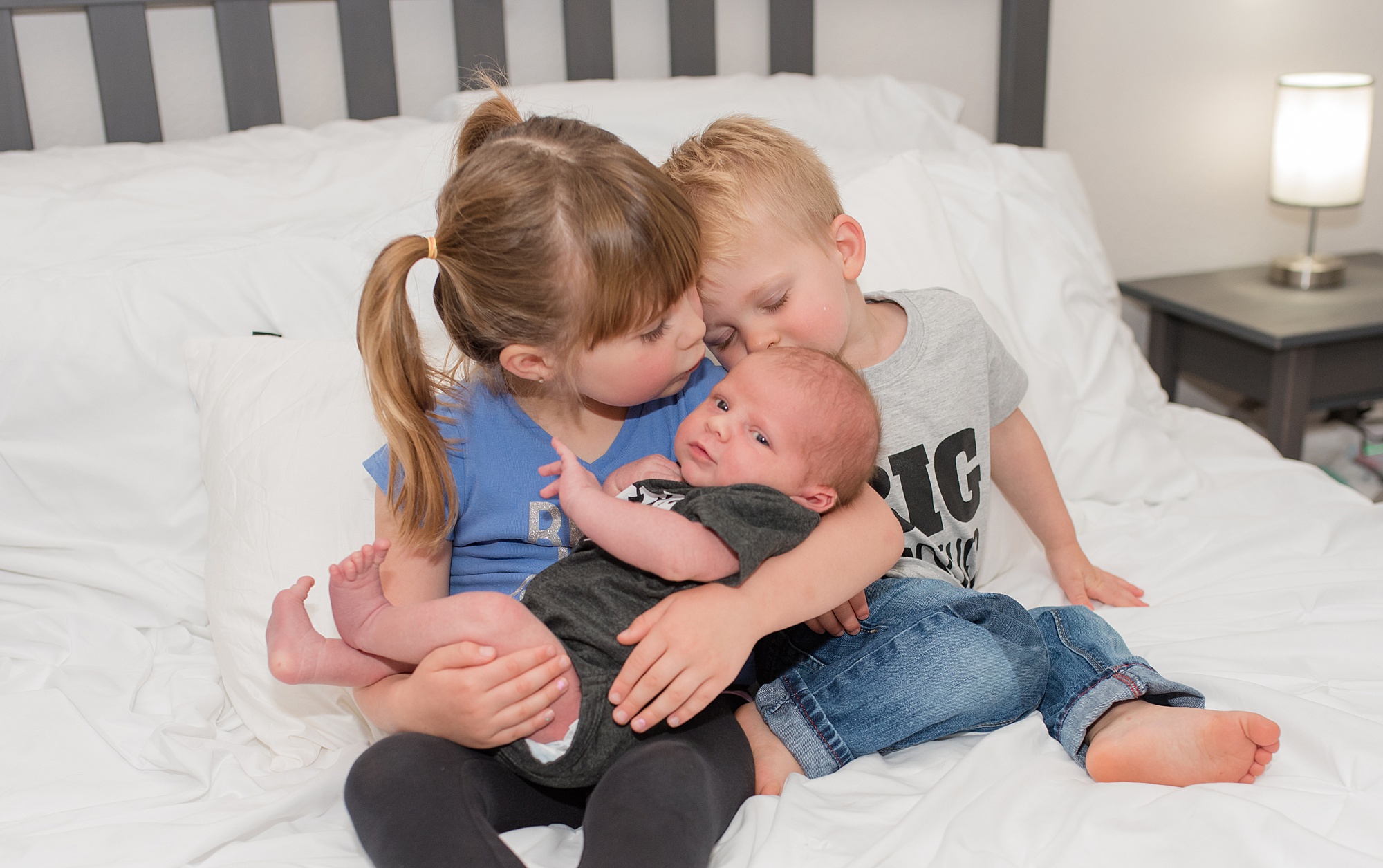 older siblings kiss the head of their newborn brother