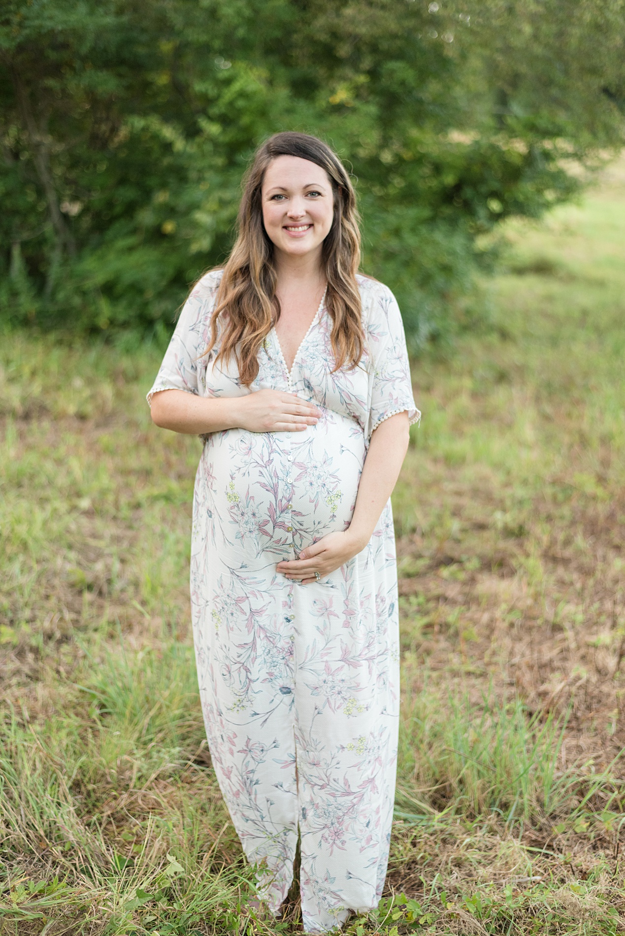 woman in floral summer dress shows off pregnant belly