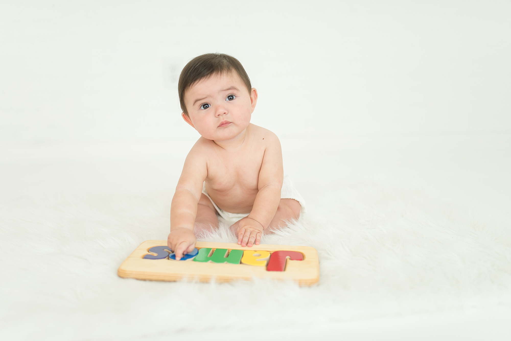 infant boy plays with his wooden name puzzle
