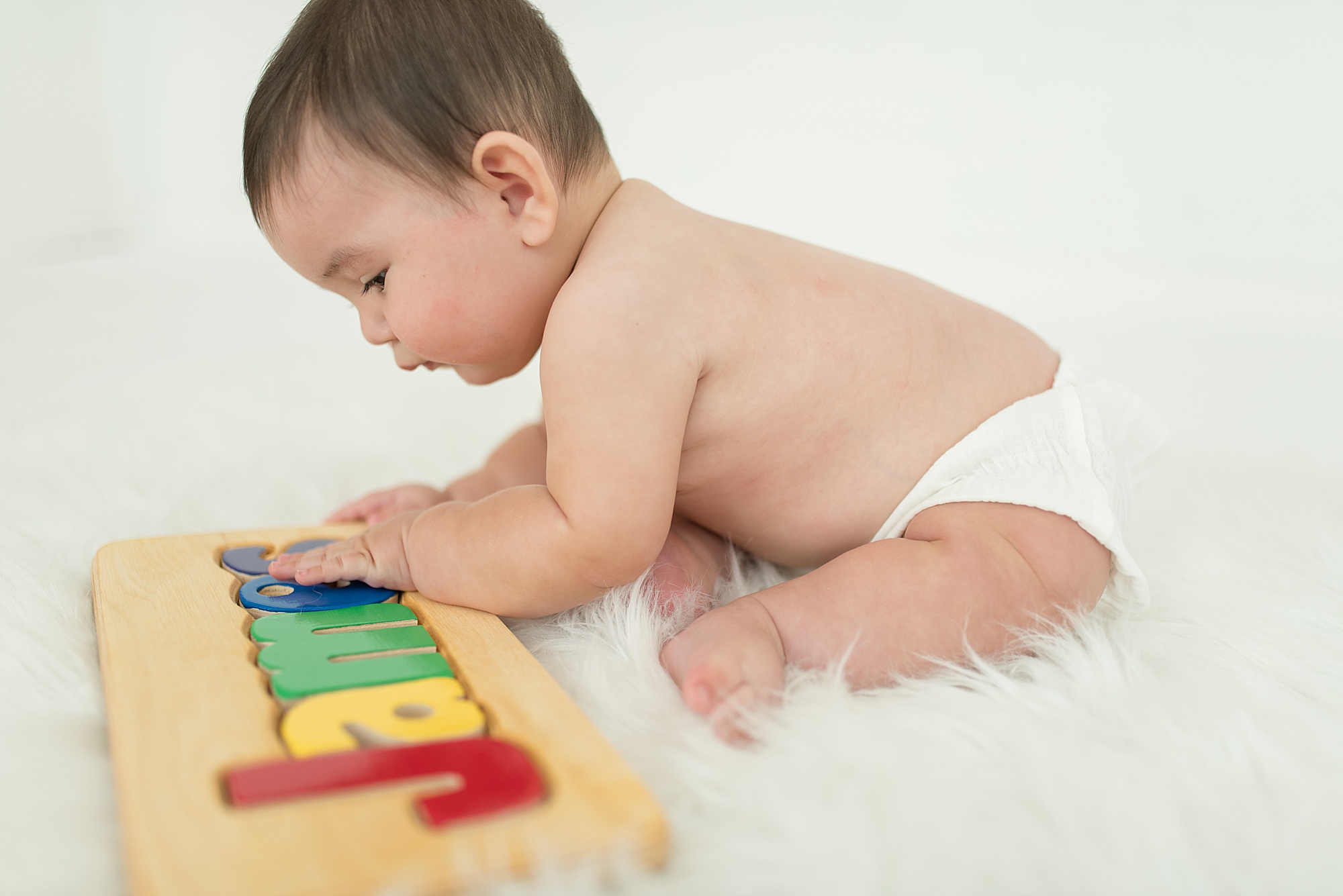 infant boy plays with his wooden name puzzle during milestone session by TX newborn photographer