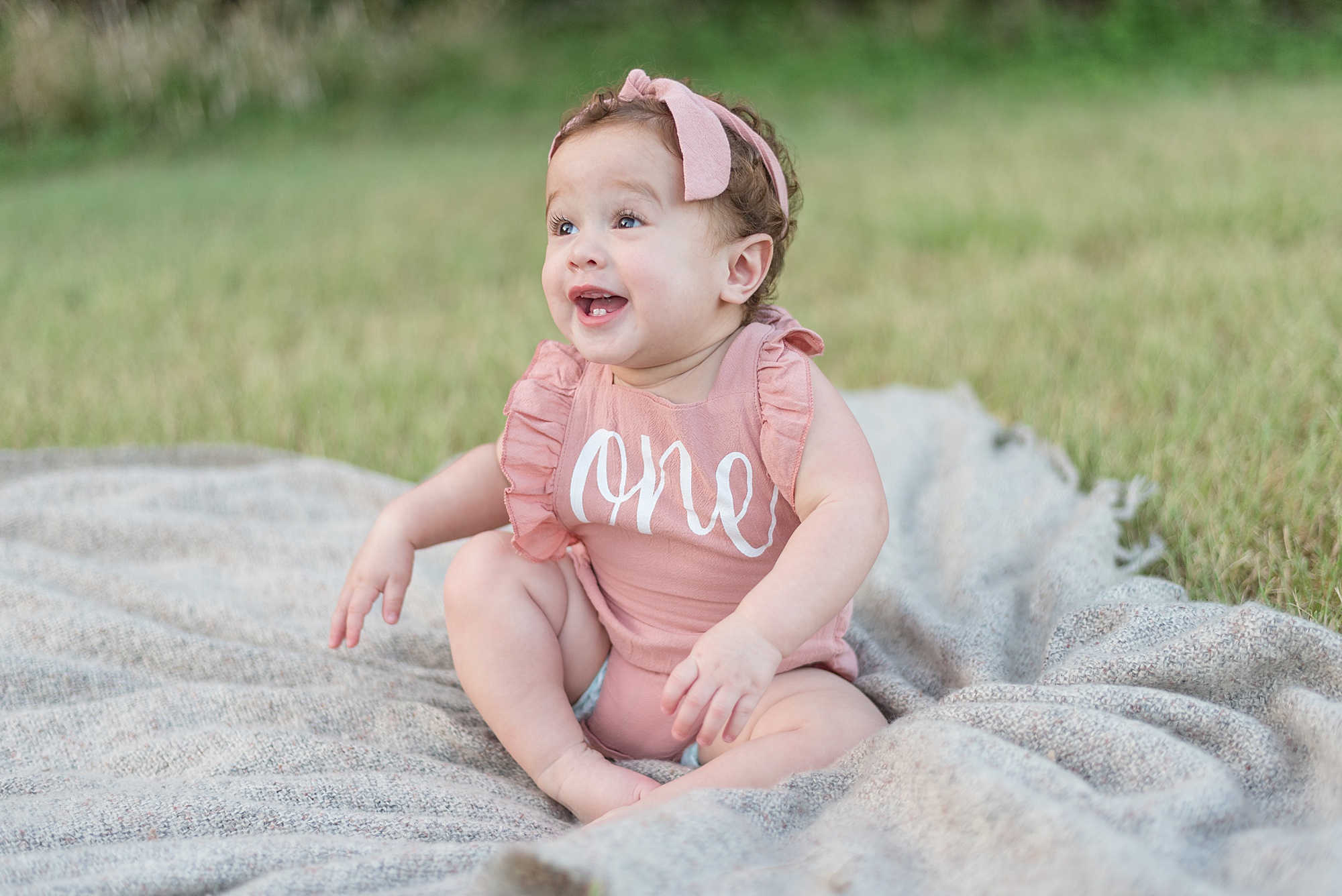 one year old sits on blanket with huge smile during milestone portraits