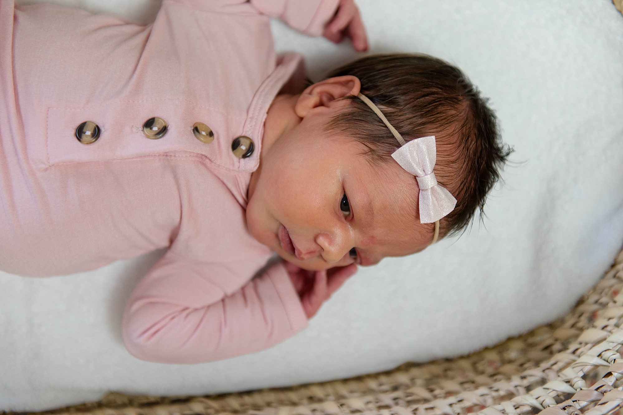 newborn girl in woven basket dressed pink onesie and white bow