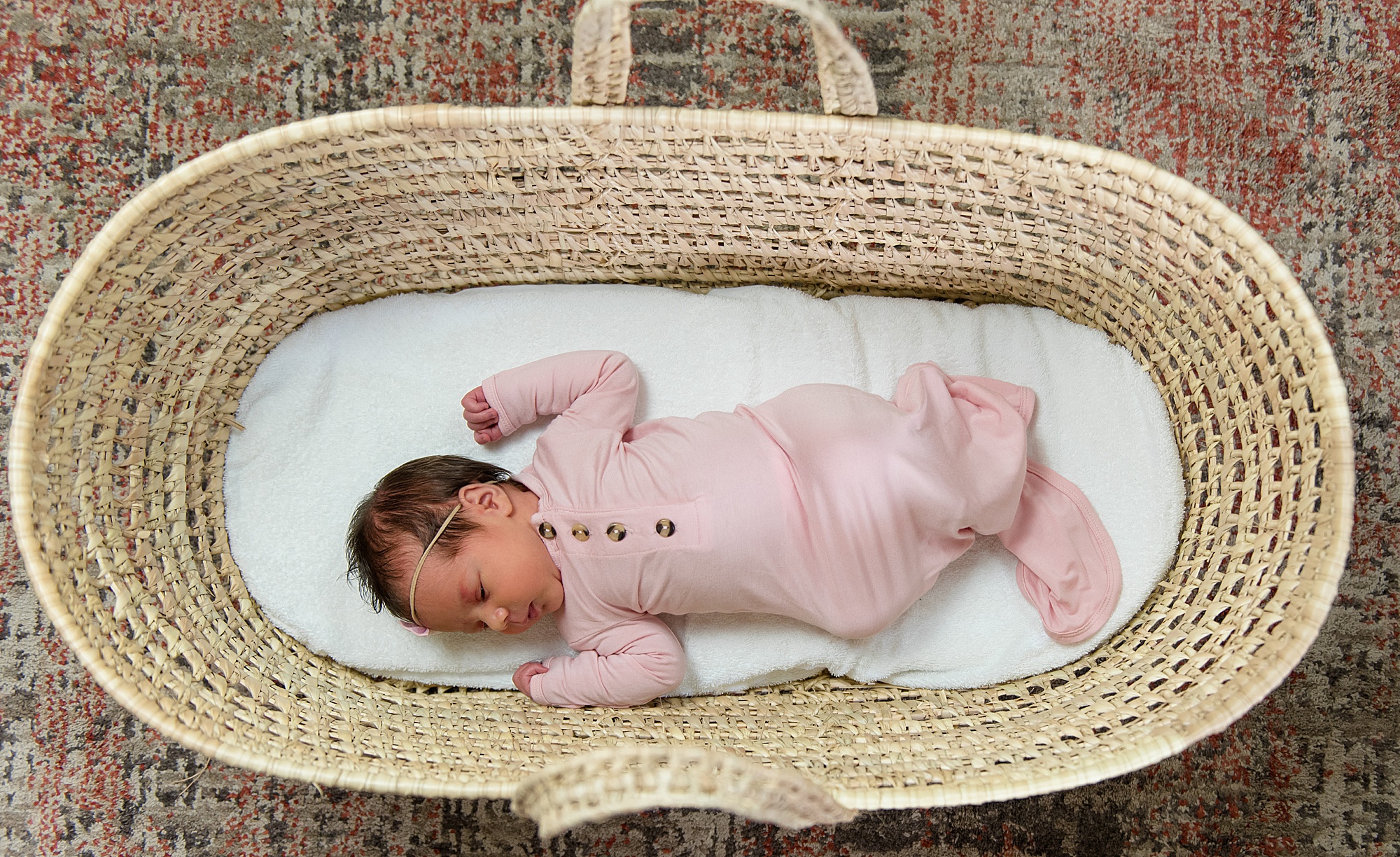 newborn girl in woven basket dressed pink onesie