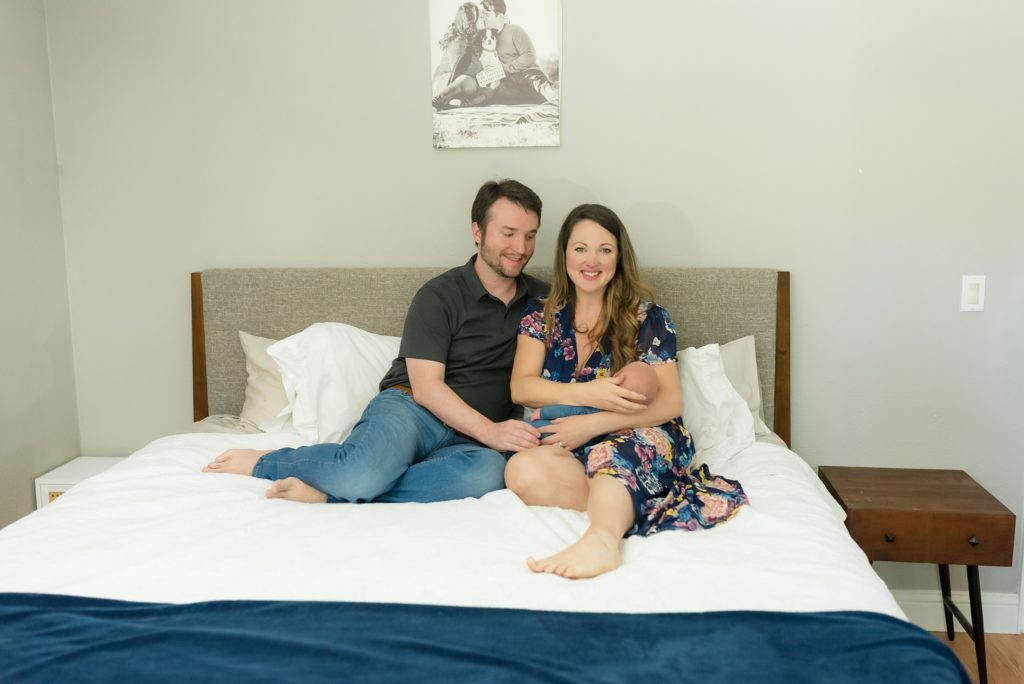 family of three sits on bed during in-home lifestyle newborn session 