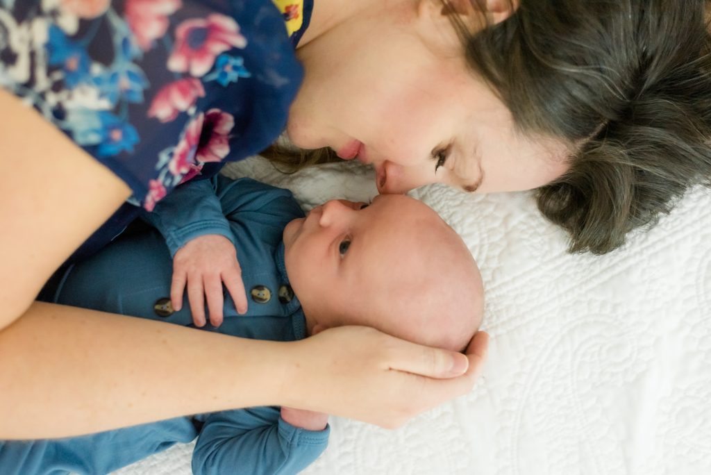 mom cuddles newborn son laying on bed during in-home newborn session