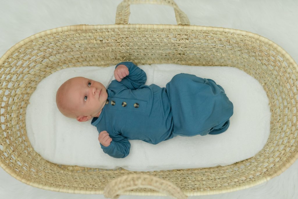 newborn dressed in dark teal laying in woven basket 