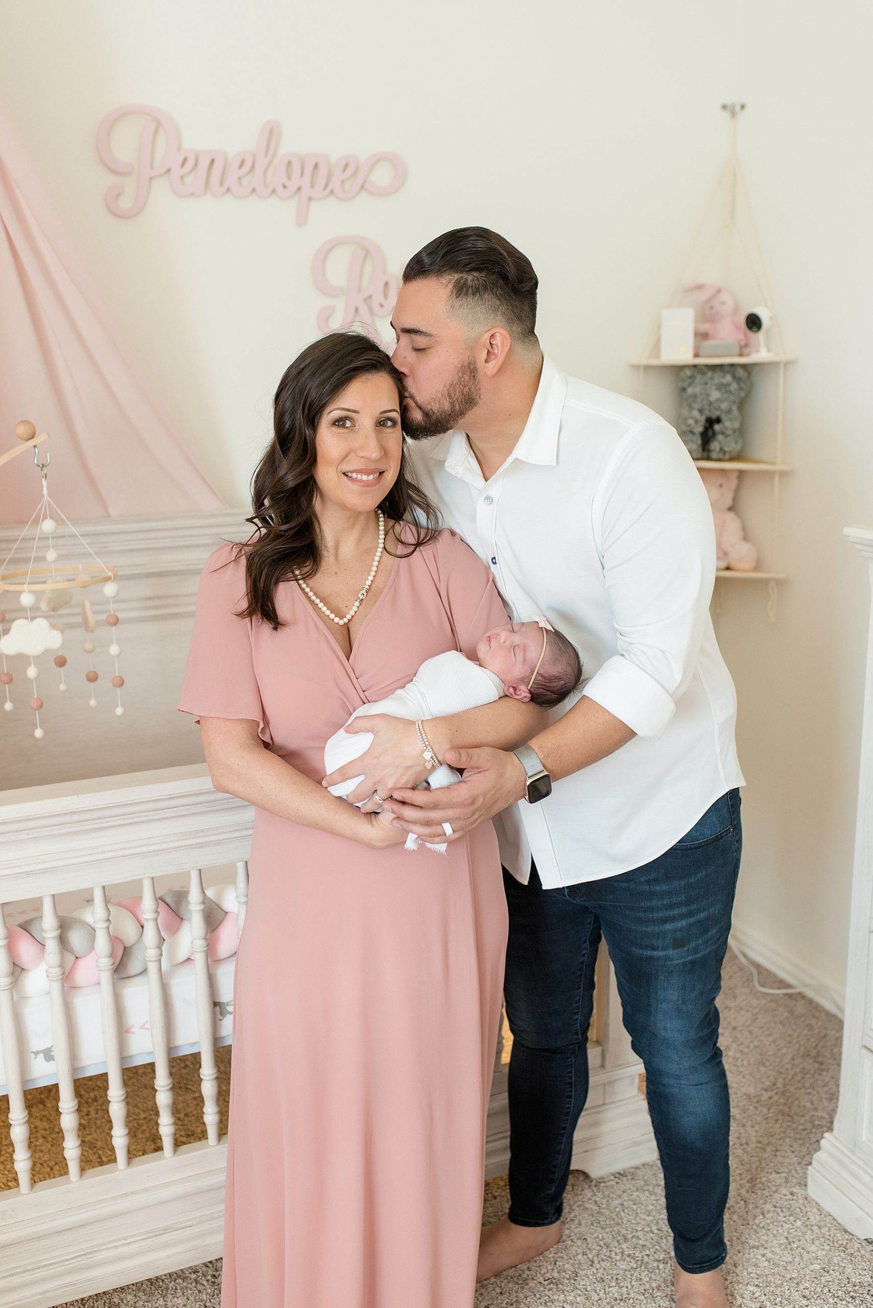 Mom and dad holding newborn baby girl in pink and white nursery | In-Home Newborn Photo Session | Lindsey Dutton Photography | Dallas Area Family Photographer | newborn session, newborn posing ideas, newborn photos, girl nursery inspiration | via lindseyduttonphotography.com