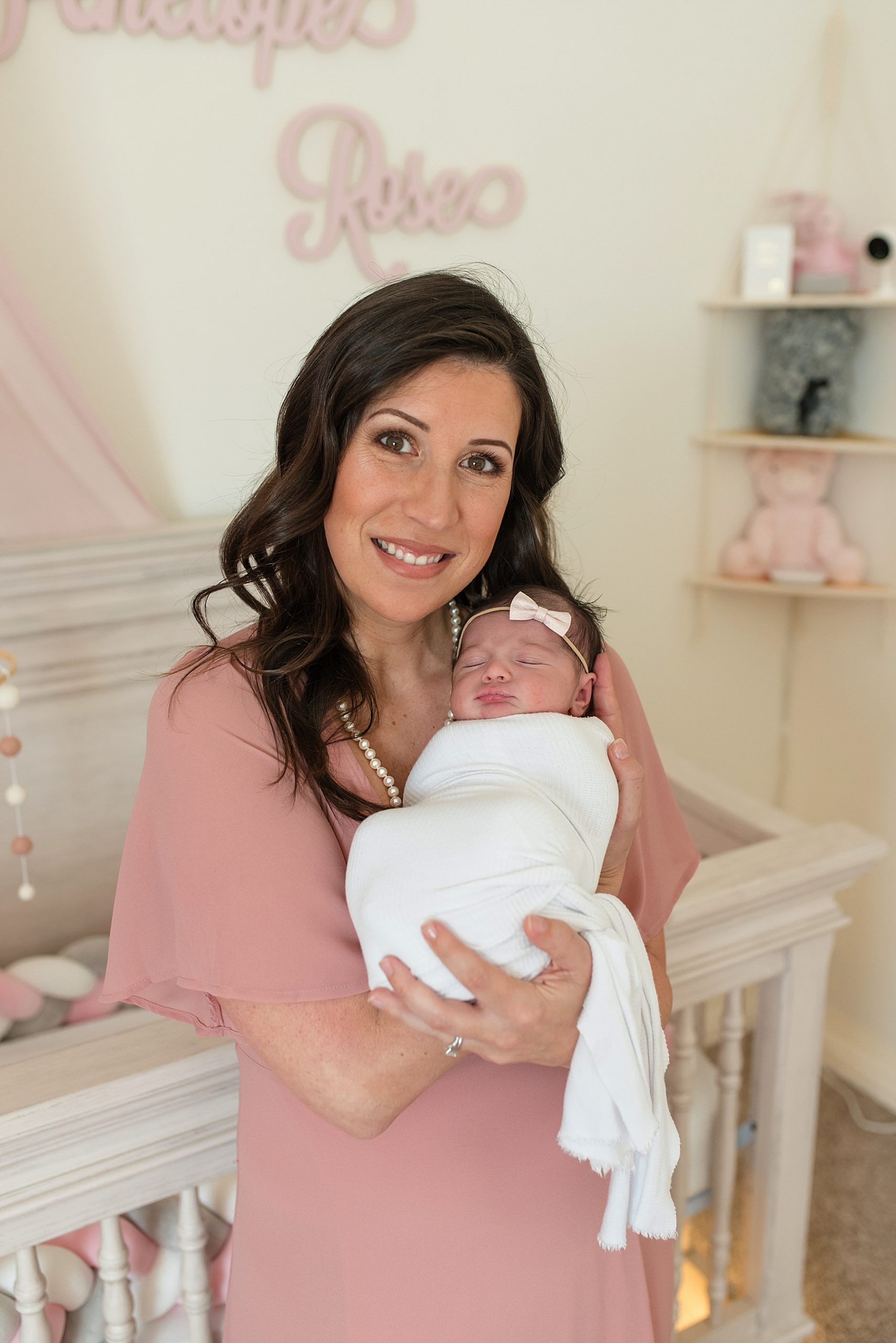 Mom holding newborn baby girl in pink and white nursery | In-Home Newborn Photo Session | Lindsey Dutton Photography | Dallas Area Family Photographer | newborn session, newborn posing ideas, newborn photos, girl nursery inspiration | via lindseyduttonphotography.com