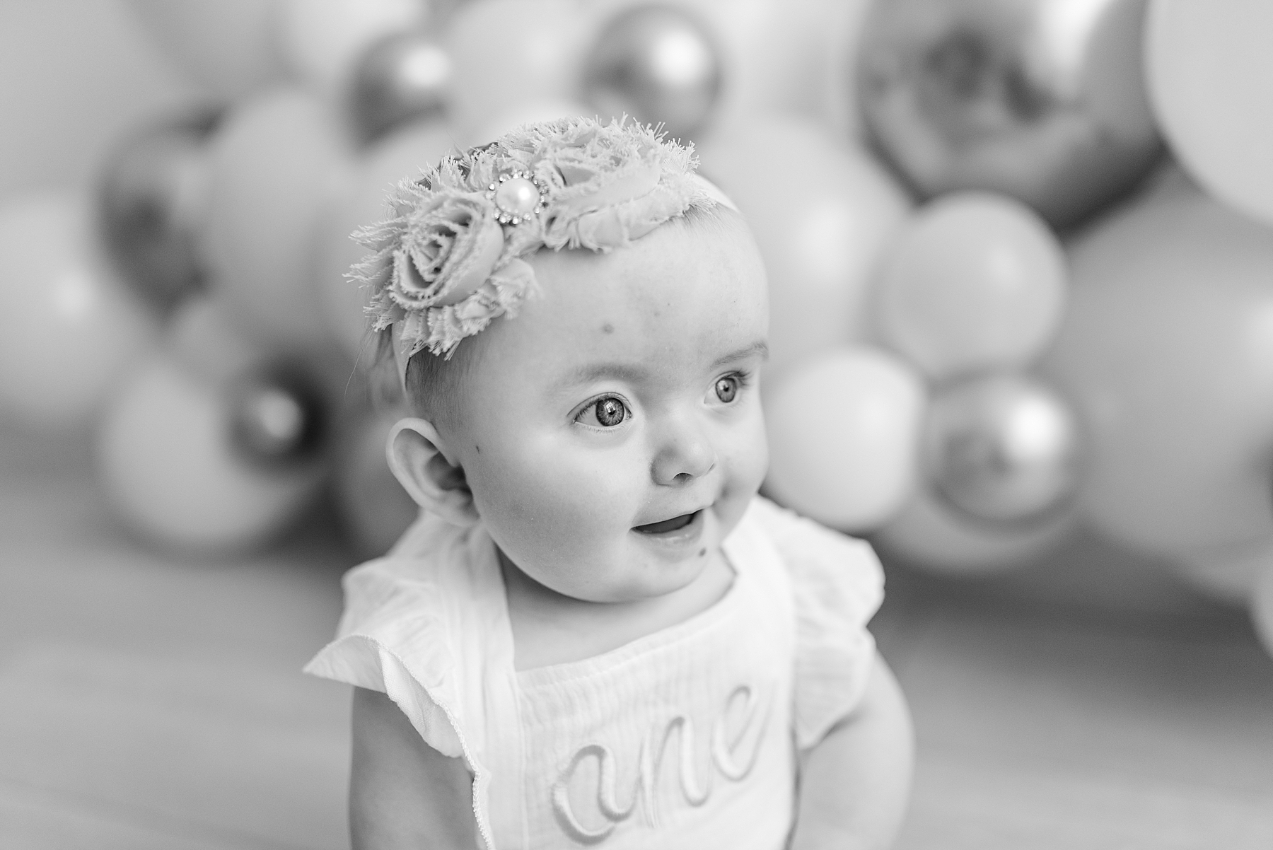 Black and White photo of little girl sitting in front of balloons. Photographed by Dallas newborn photographer Lindsey Dutton Photography