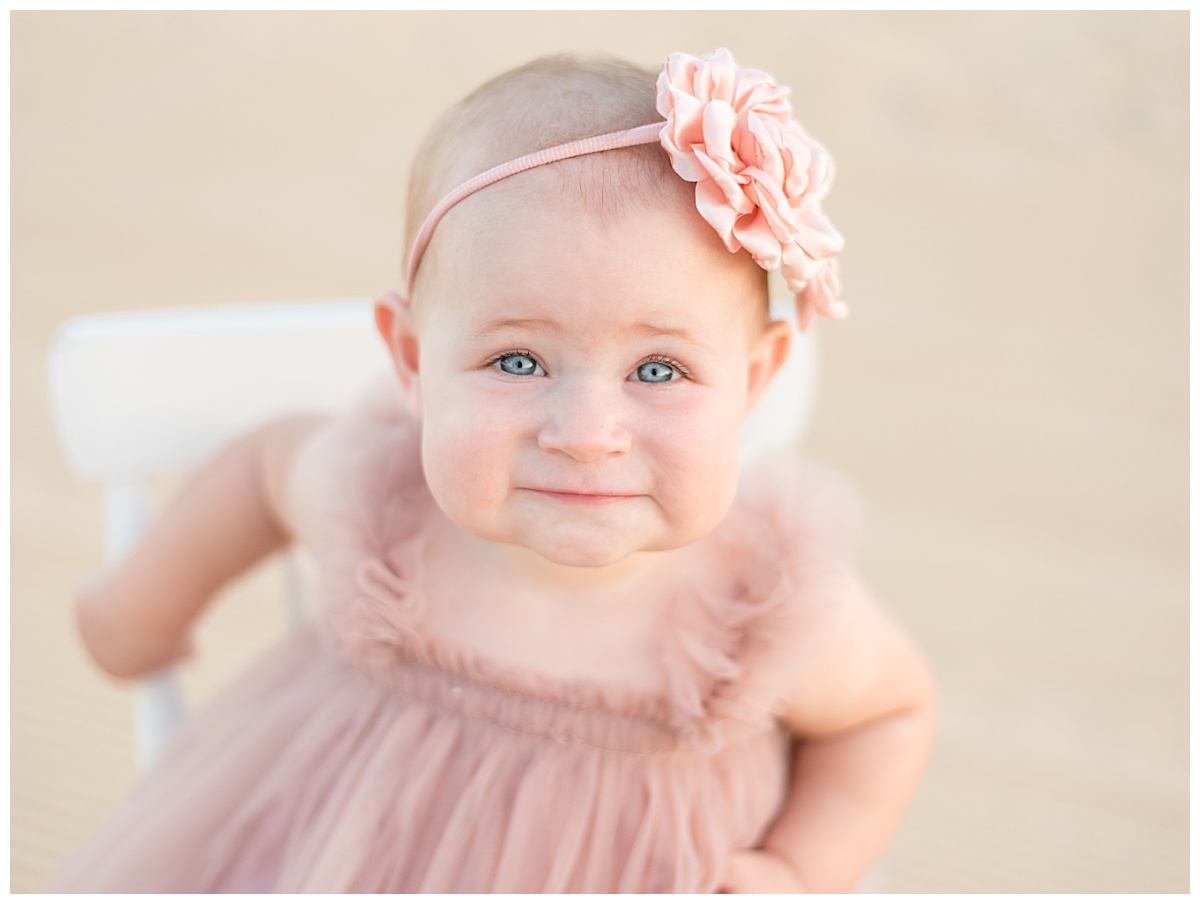 Baby girl in pink tulle dress smiles up at the camera for her cake smash photos in North Dallas by Lindsey Dutton Photography, a Dallas Cake Smash Photographer. 