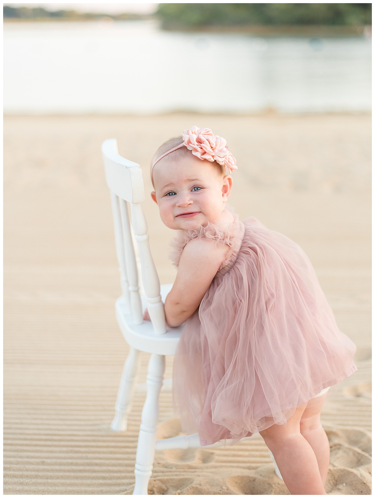 One year old girl leaning on a white chair on the beach for her cake smash pictures in North Dallas by Lindsey Dutton Photography, a Dallas Cake Smash Photographer. 