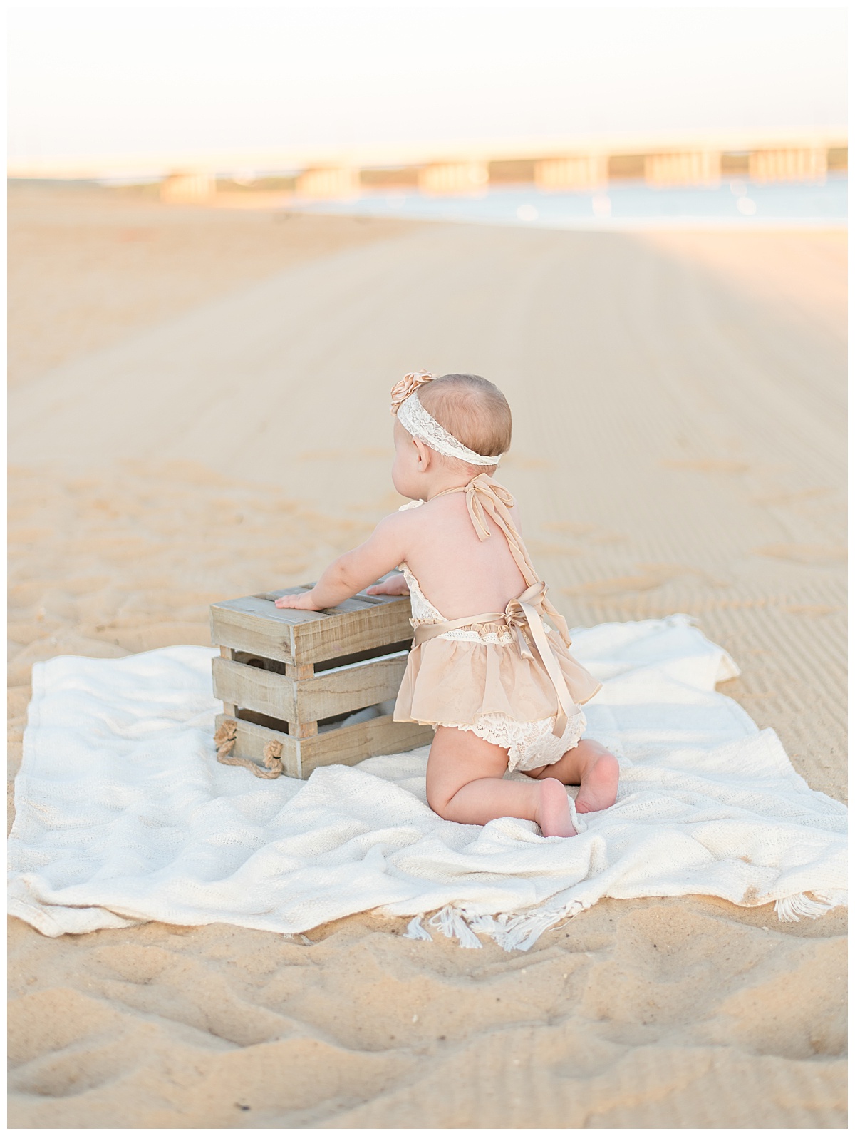Baby girl pulling herself up on a crate at the beach for her cake smash portraits in North Dallas by Lindsey Dutton Photography, a Dallas Cake Smash Photographer. 