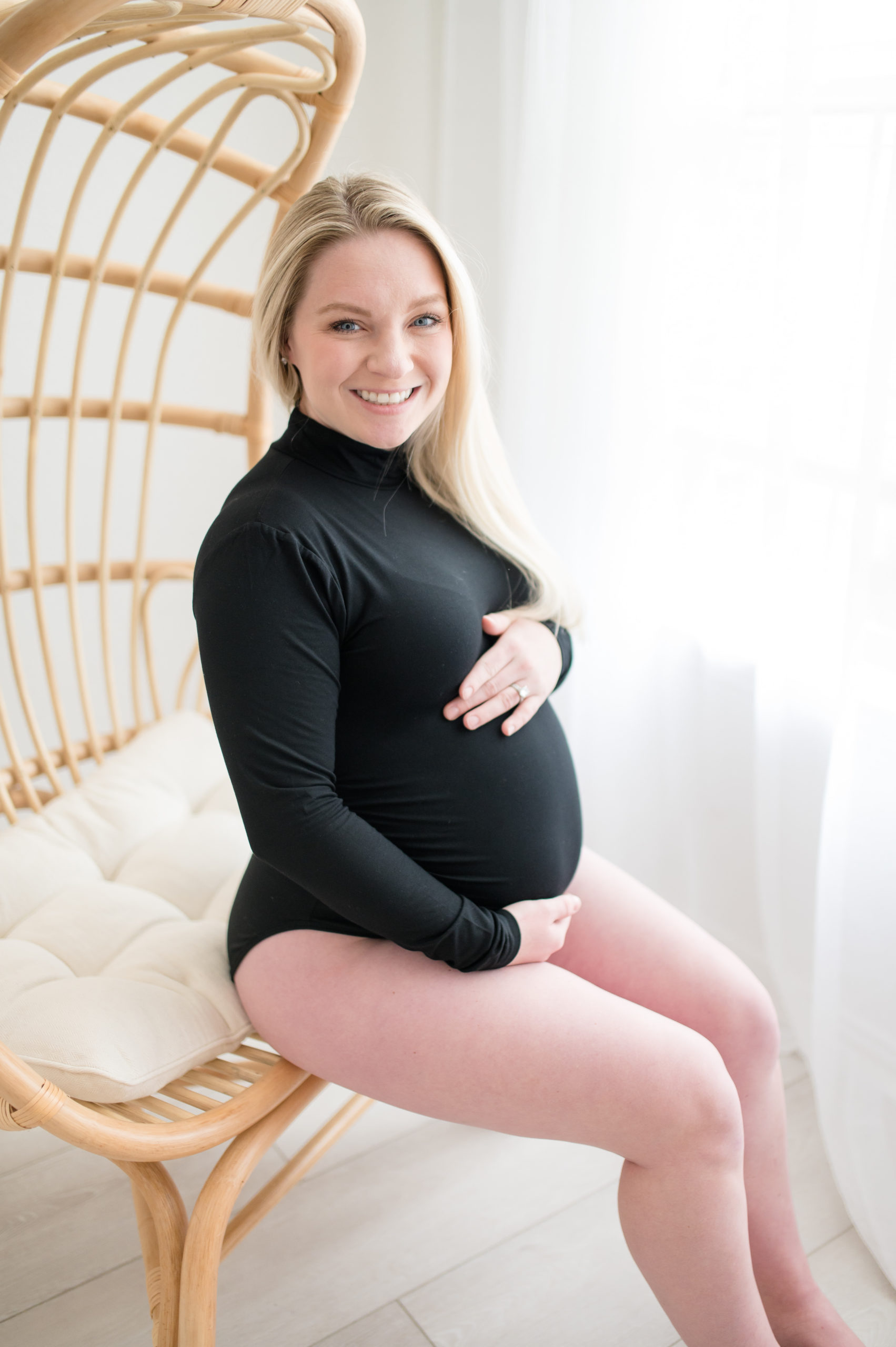 pregnant women in black body suit in a classy in studio maternity session sitting in a chair 