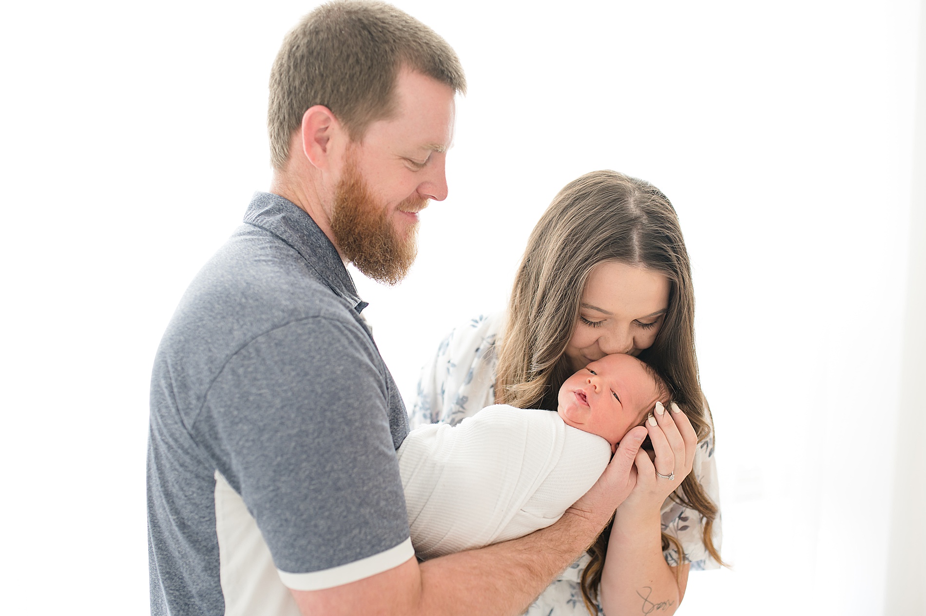 parents hold and kiss their newborn during studio session