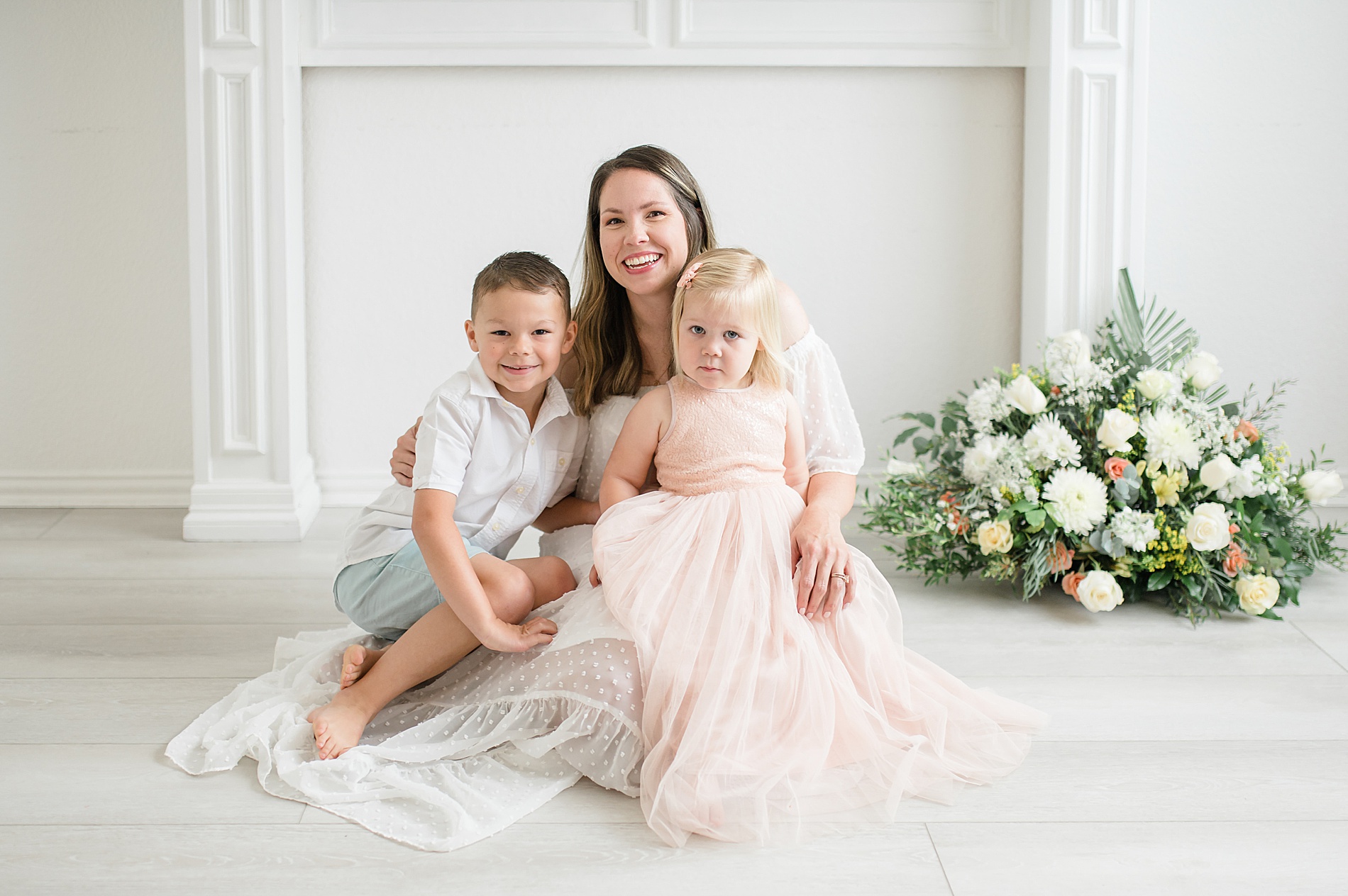 mama sits with her two kids at light and airy Dallas TX studio photographed by Lindsey Dutton Photography, a Dallas Newborn photographer
