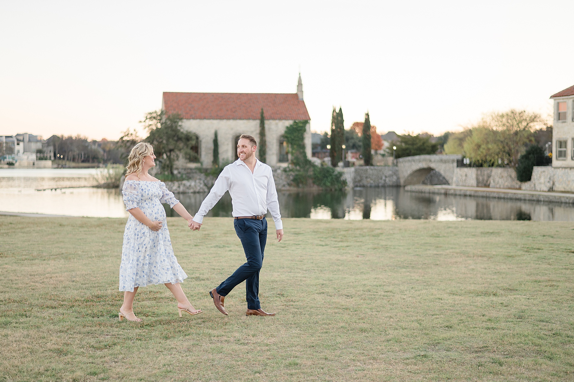 couple walk across field by lake during maternity session photographed by Lindsey Dutton Photography, a Dallas Family photographer
