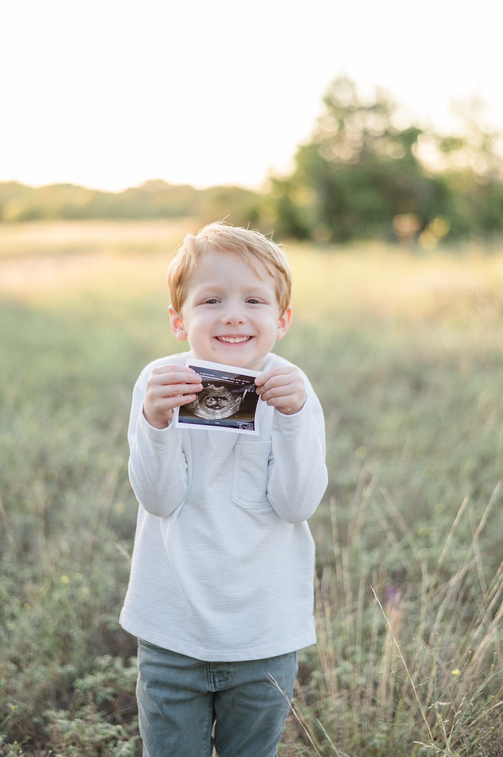 excited little boy holds ultrasound image taken by Lindsey Dutton Photography, a Dallas maternity photographer
