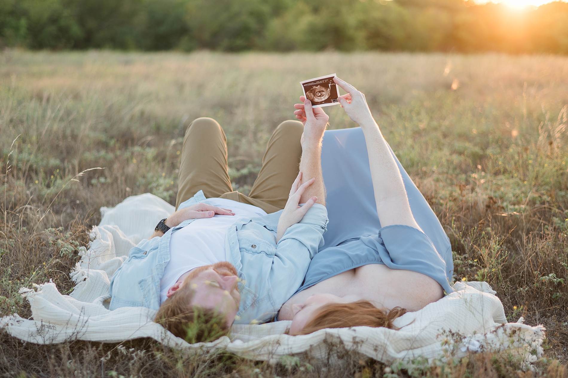 couple laying down hold up ultrasound photo during pregnancy announcement taken by Lindsey Dutton Photography, a Dallas maternity photographer

